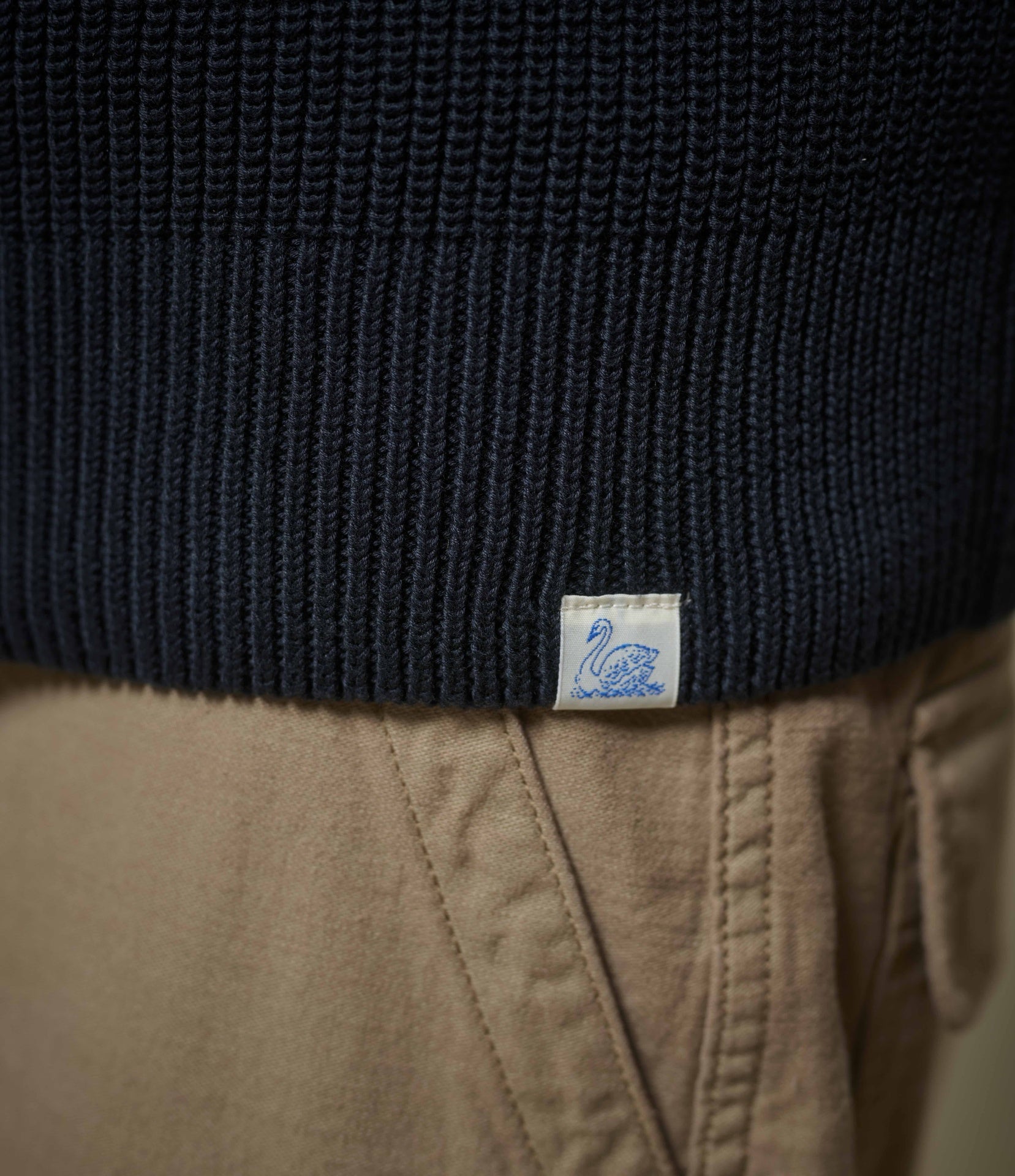 Close-up of a black sweater with a visible brand label on beige pants.