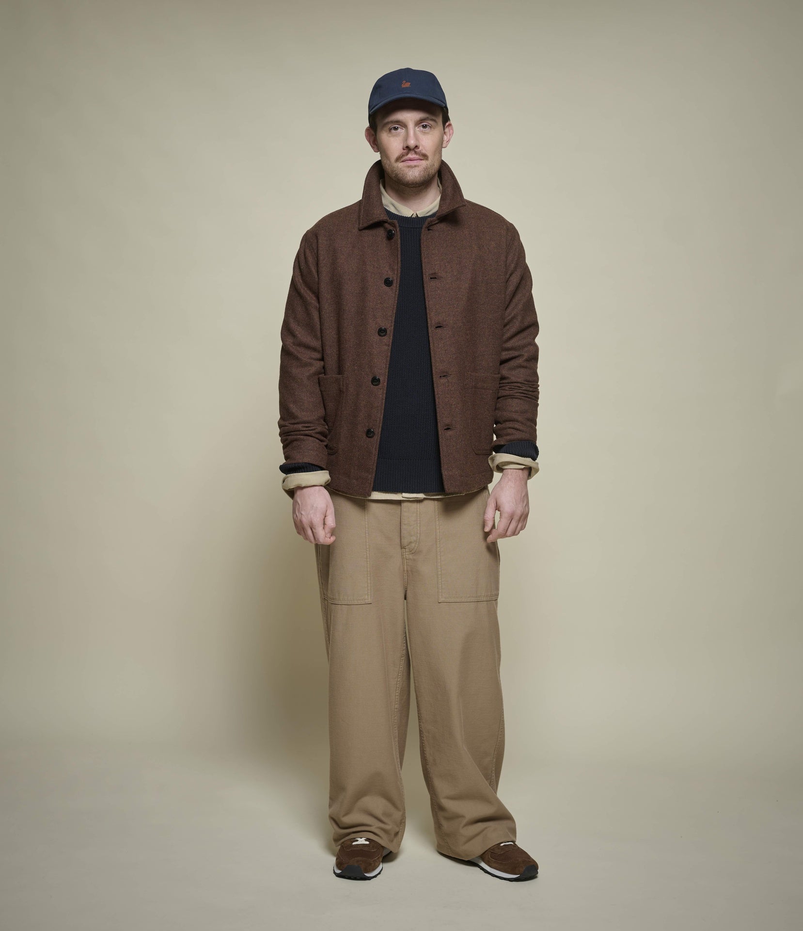 Man wearing a brown jacket and beige pants against a beige background