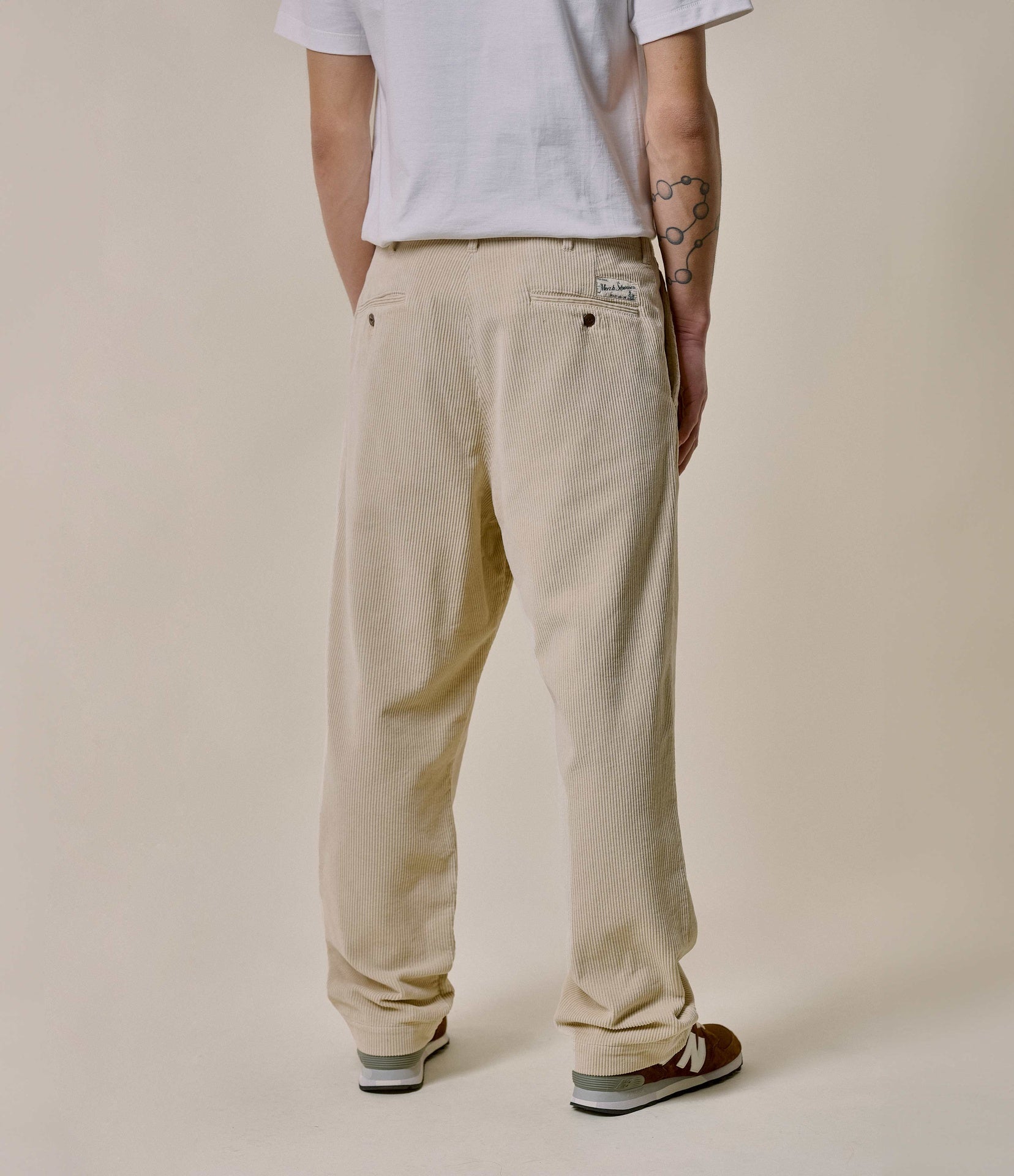 Person wearing beige pants and a white shirt against a plain background.