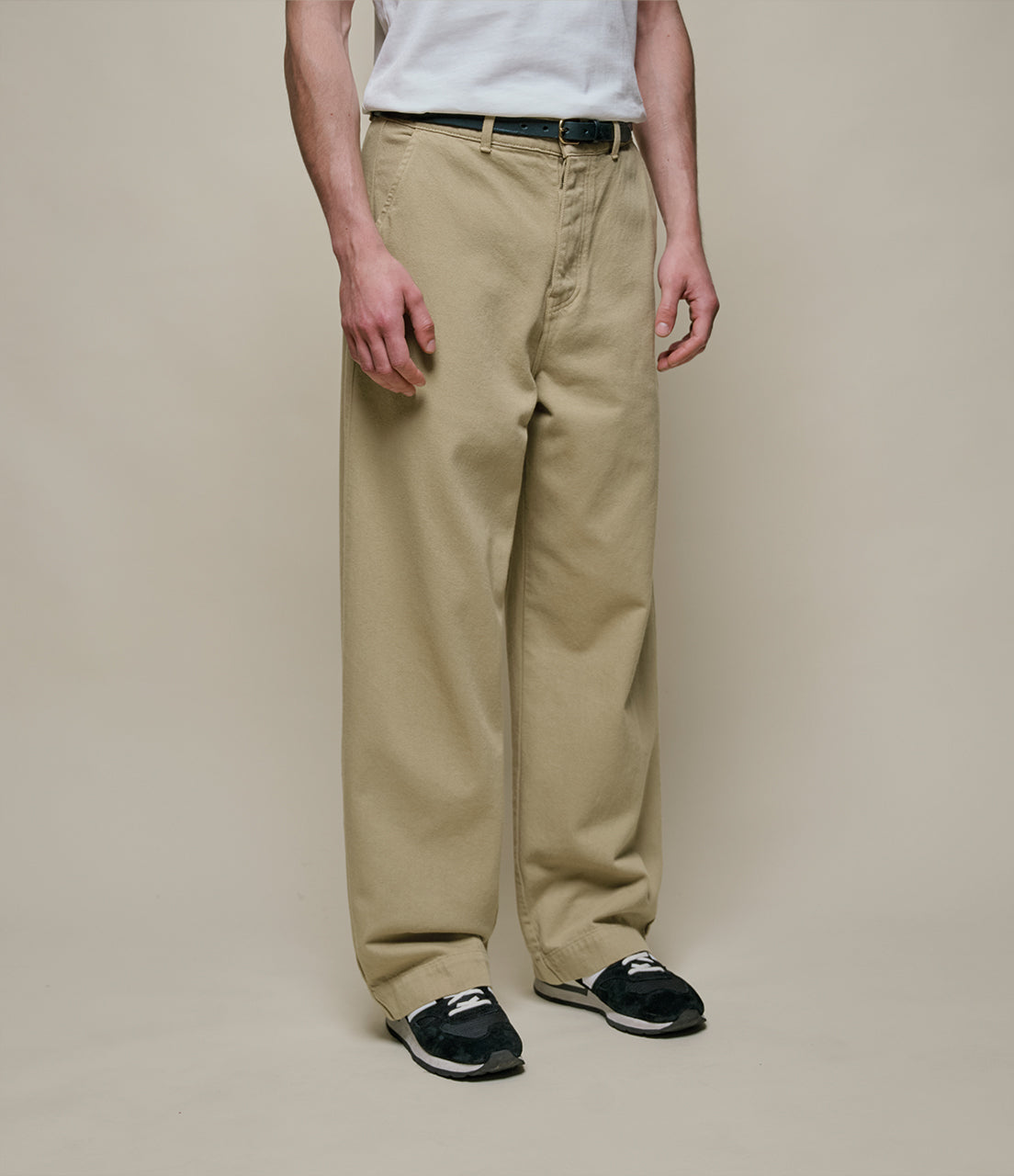 Person wearing beige pants and black shoes on a plain background