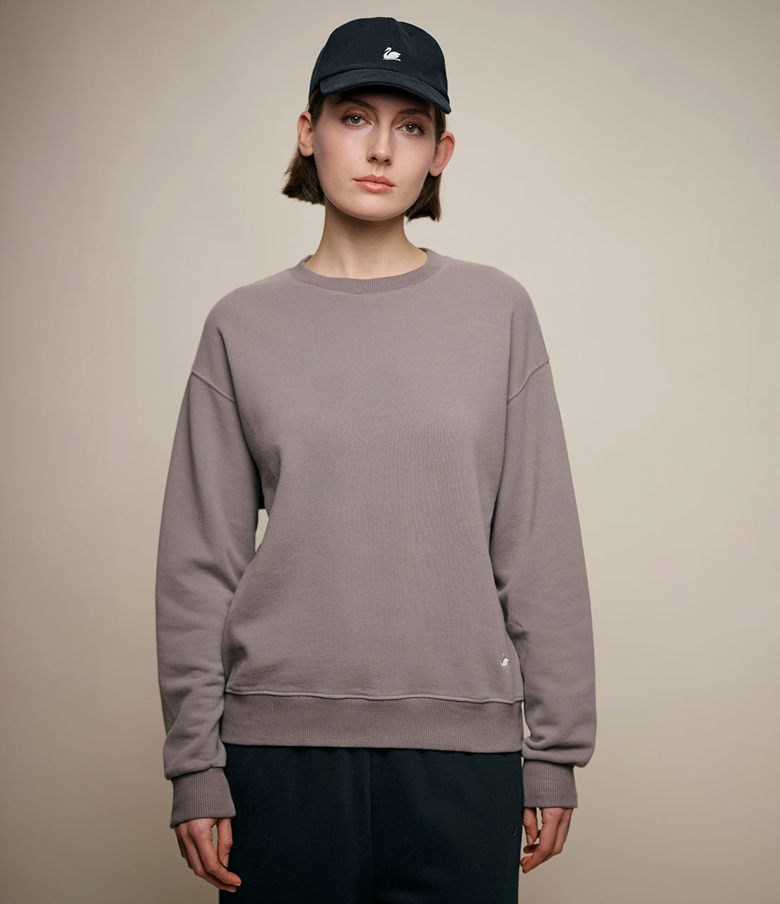 Person wearing a gray sweatshirt and black cap on a beige background