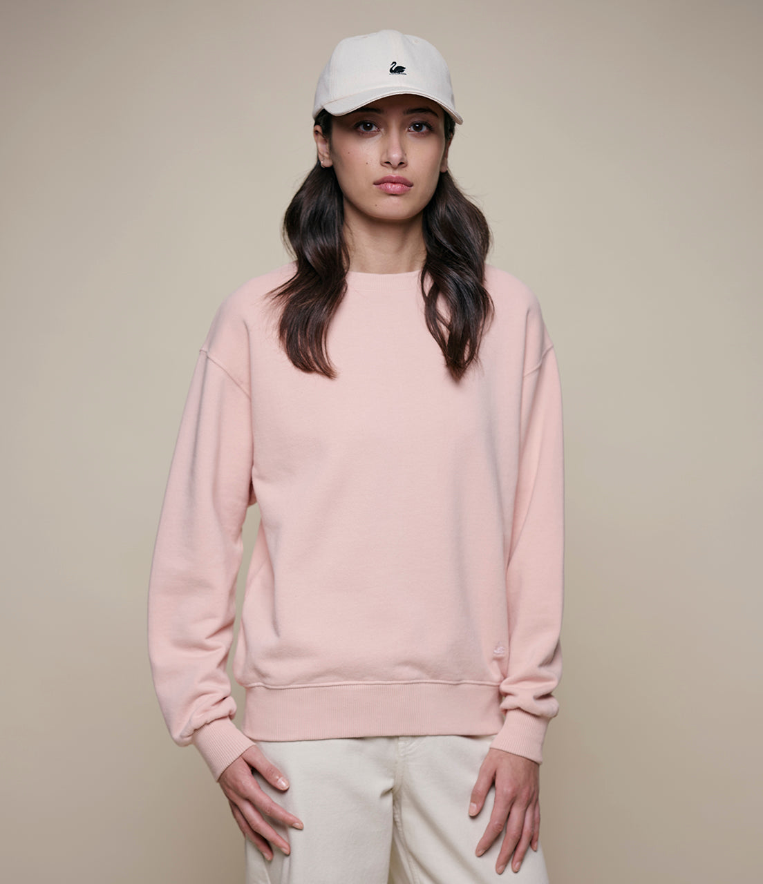 Person wearing a pink sweatshirt and white cap on a beige background
