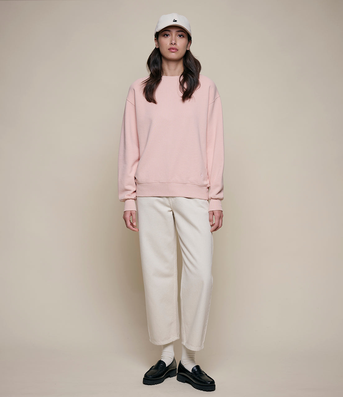 Person wearing a pink sweatshirt, white pants, and black shoes on a beige background