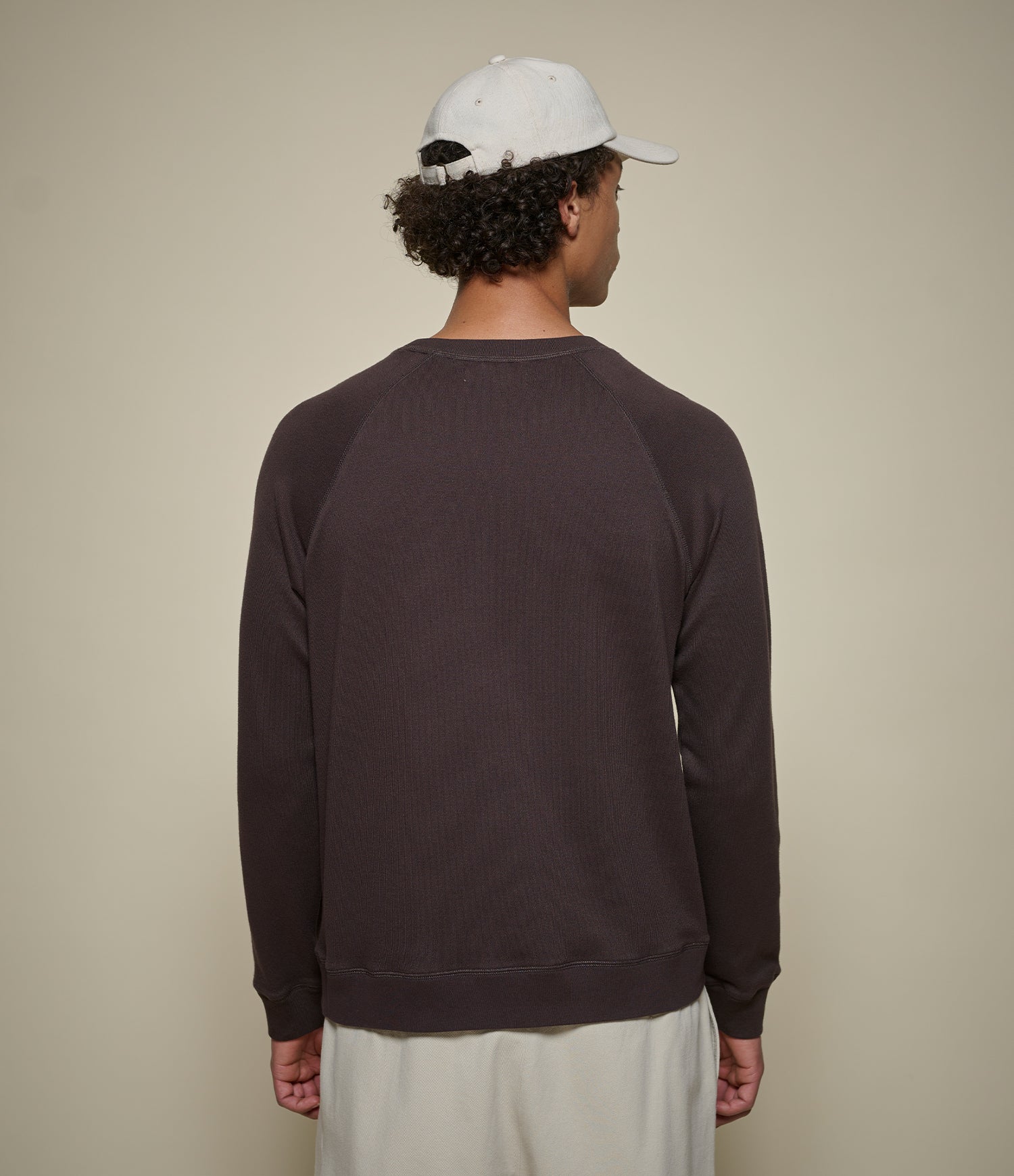 Person wearing a dark brown lightweight sweatshirt and white cap on a beige background