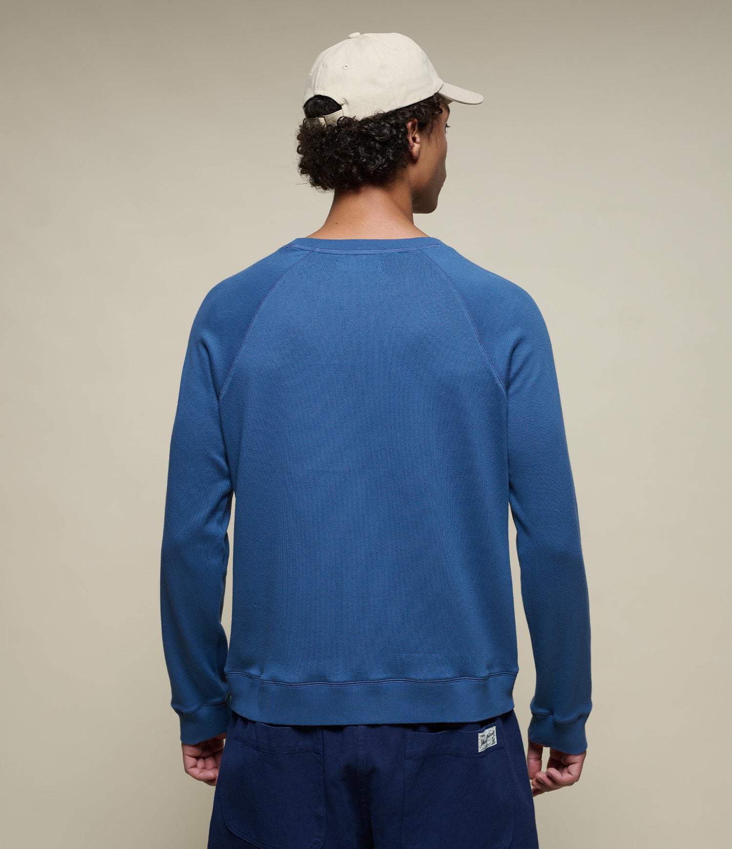 Person wearing an indigo blue sweatshirt and white cap on a beige background