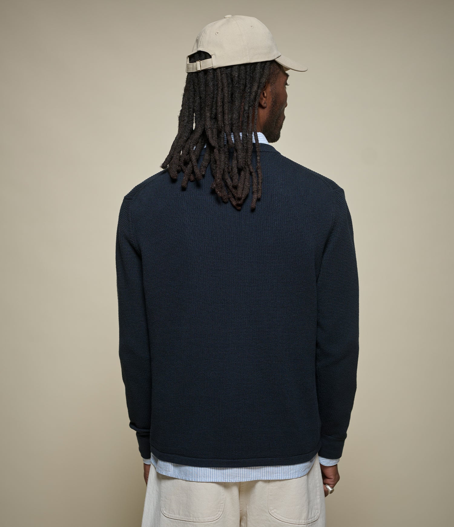 Person wearing a navy sweater and beige cap on a beige background