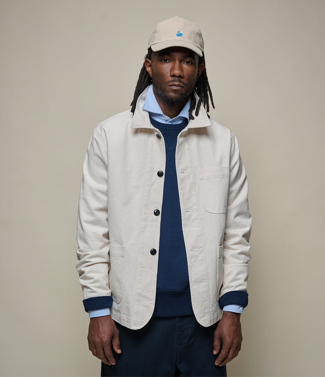 Man wearing a beige jacket and cap against a plain background