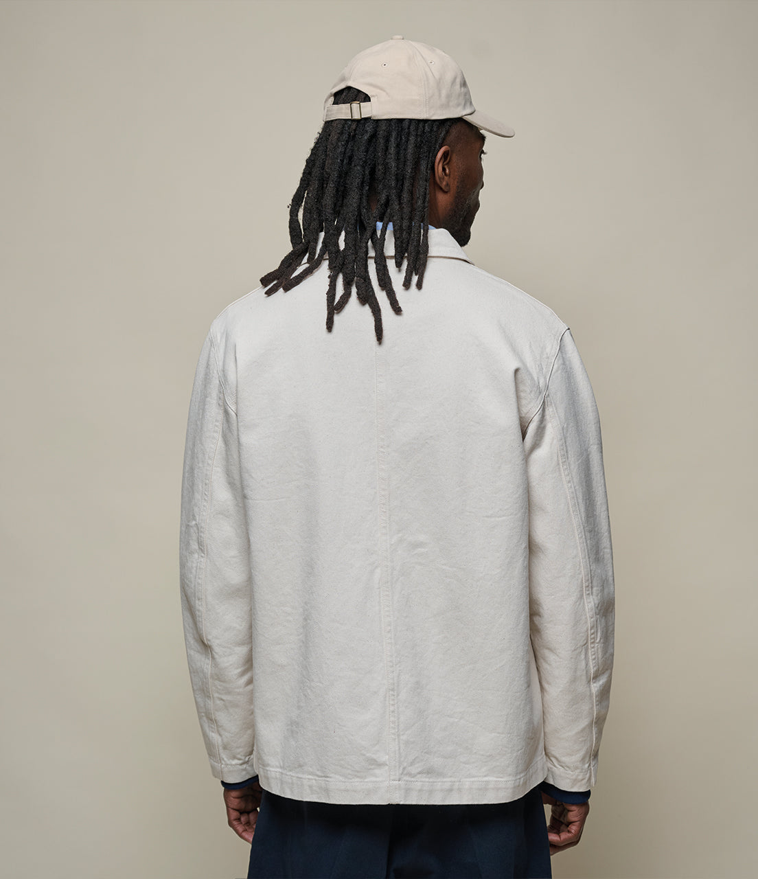 Person wearing a light gray jacket and beige cap against a plain background