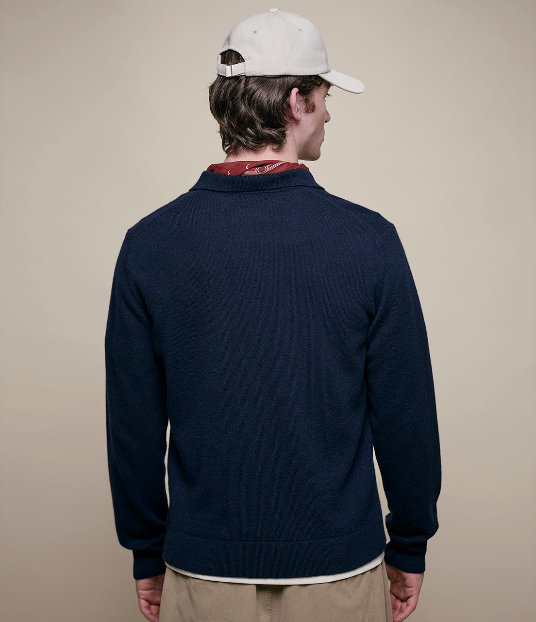 Man wearing a navy blue pullover with a beige cap on a beige background