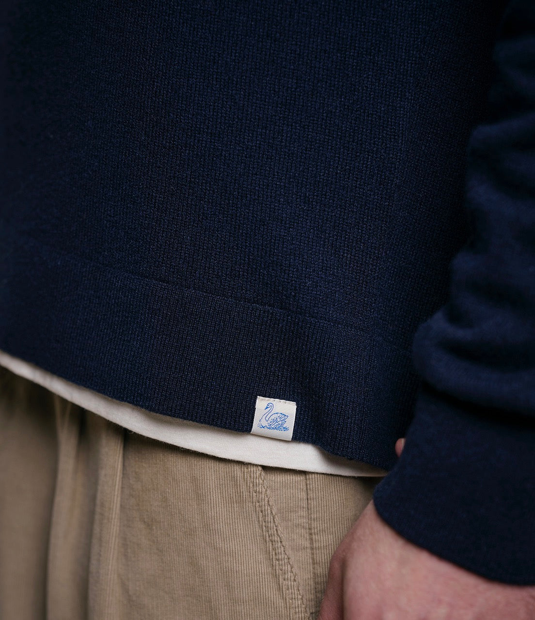 Navy sweater with a brand logo on a person wearing beige pants.