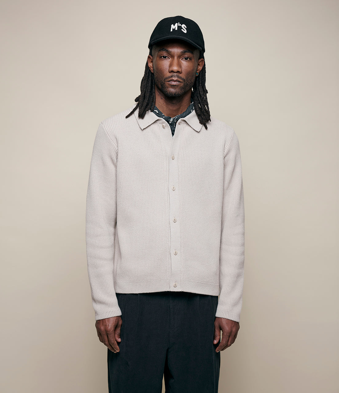 Person wearing a beige ribbed knitted shirt and a black cap