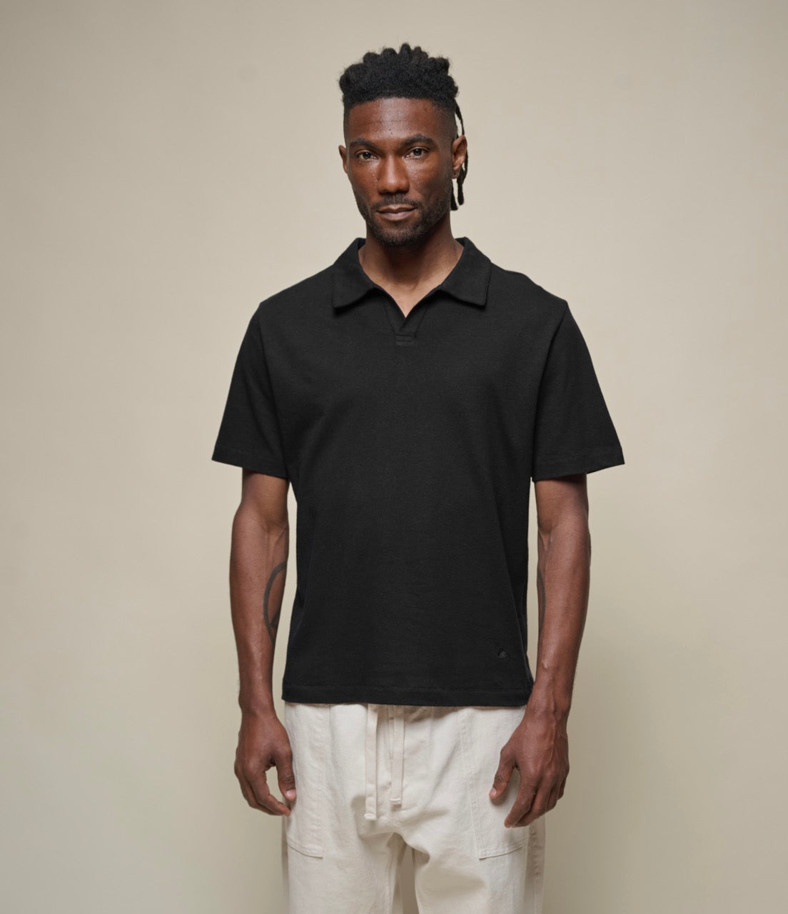 A man wearing a black short sleeve linen polo shirt with a collar, paired with light-colored pants.