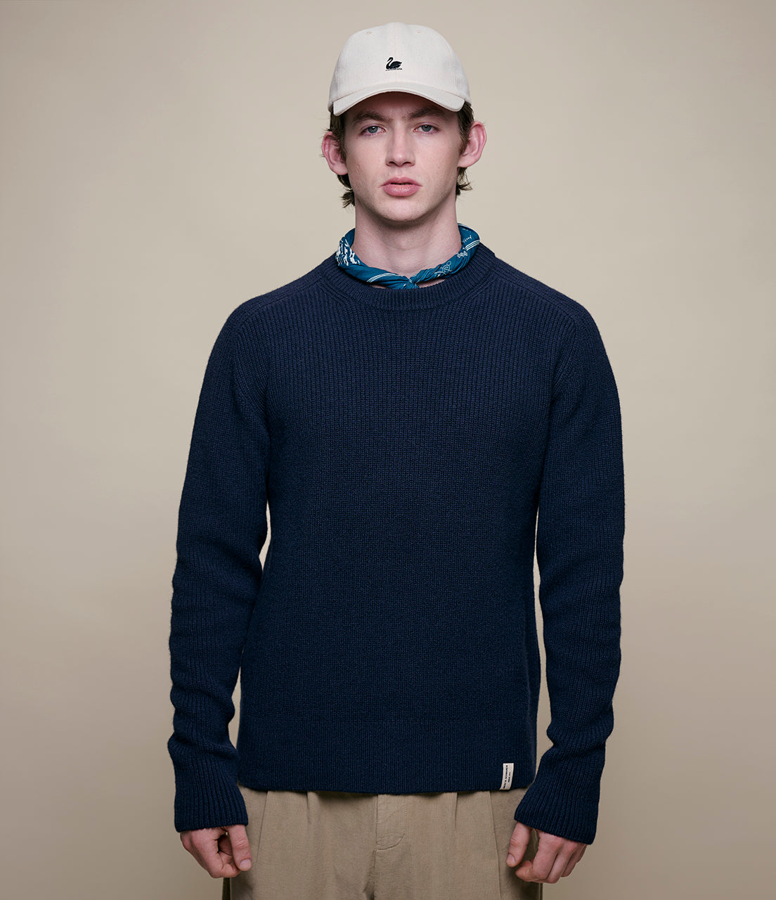 Man wearing a navy sweater and beige cap against a beige background