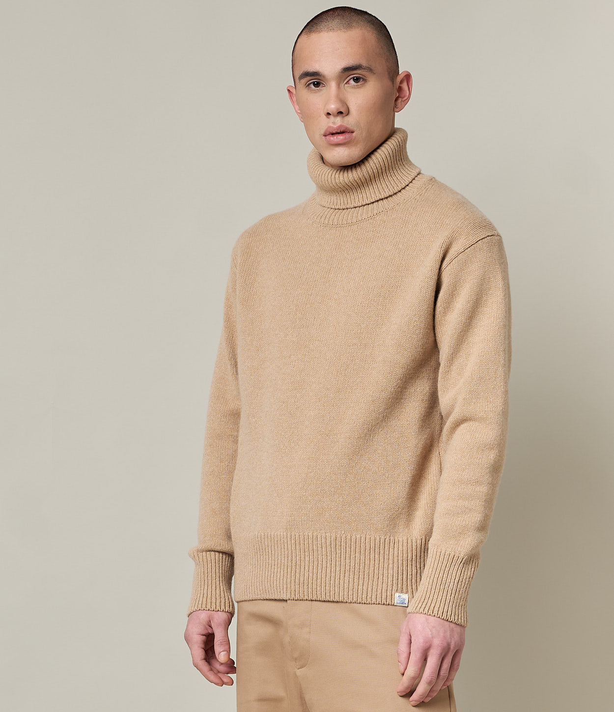 Man wearing a beige turtleneck sweater against a plain background