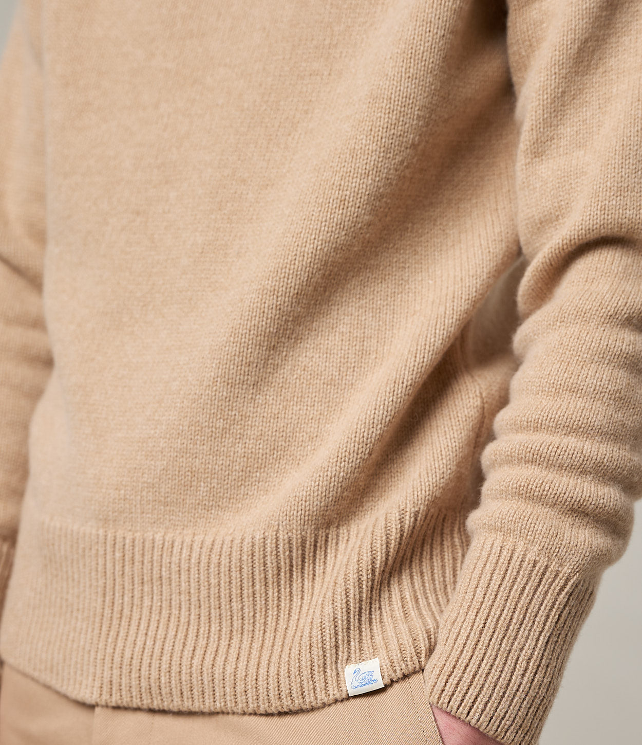 Close-up of a beige sweater with a brand label on a neutral background