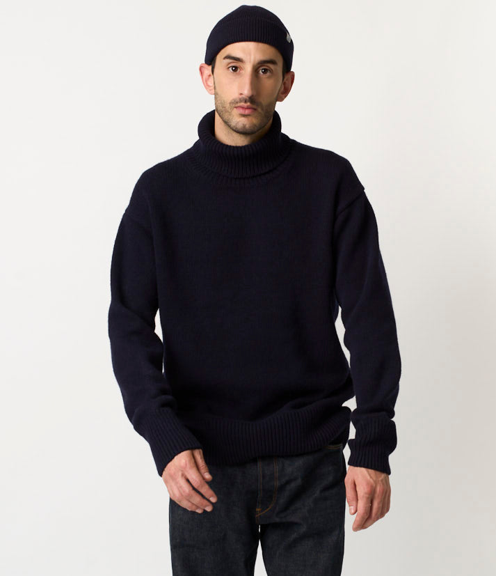Man wearing a black turtleneck sweater and dark pants on a white background