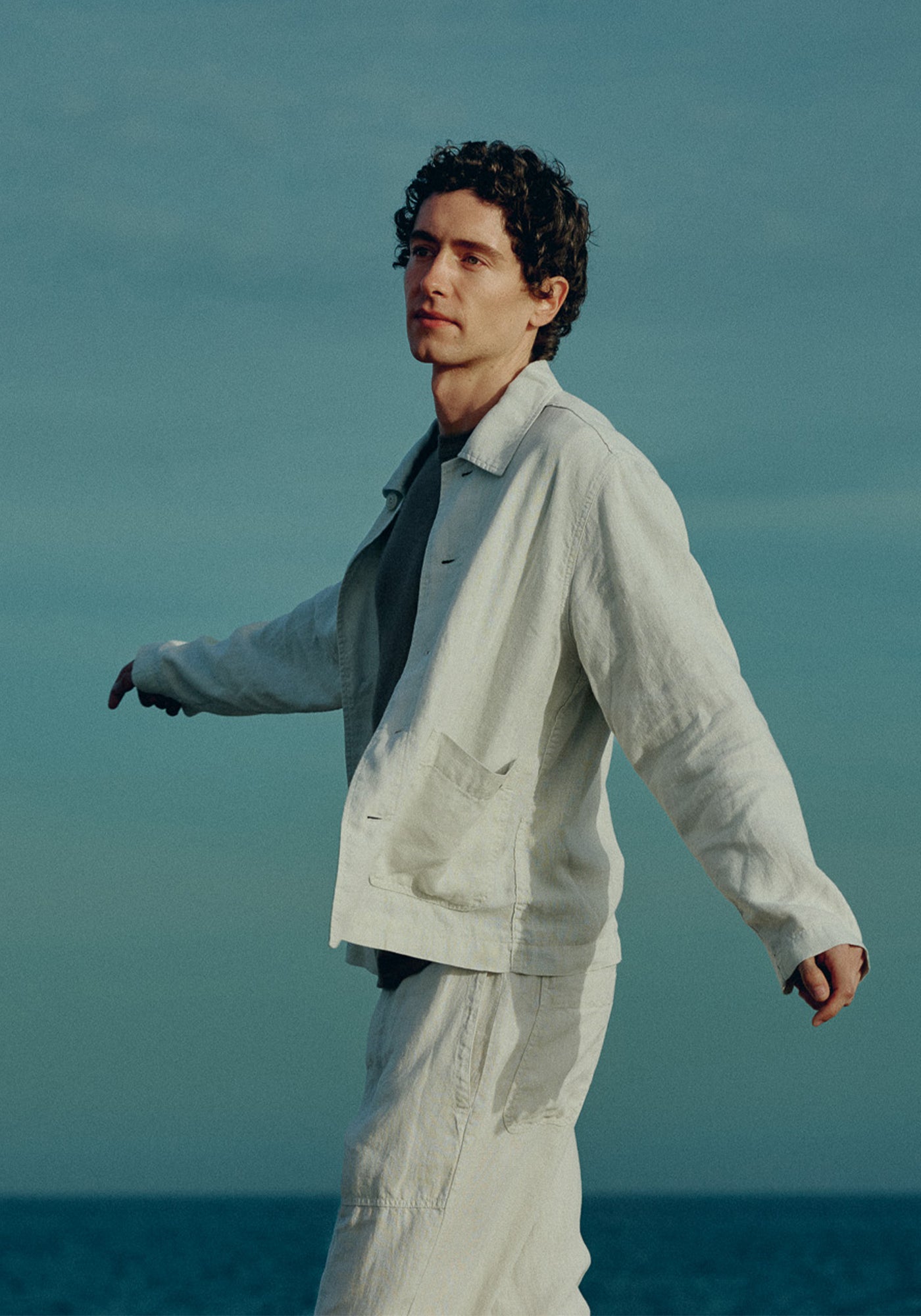 Man in light-colored linen outfit standing against a blue sky
