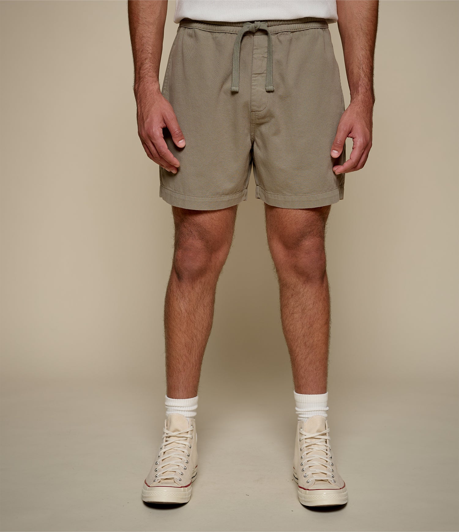 Person wearing green shorts and white sneakers on a plain background