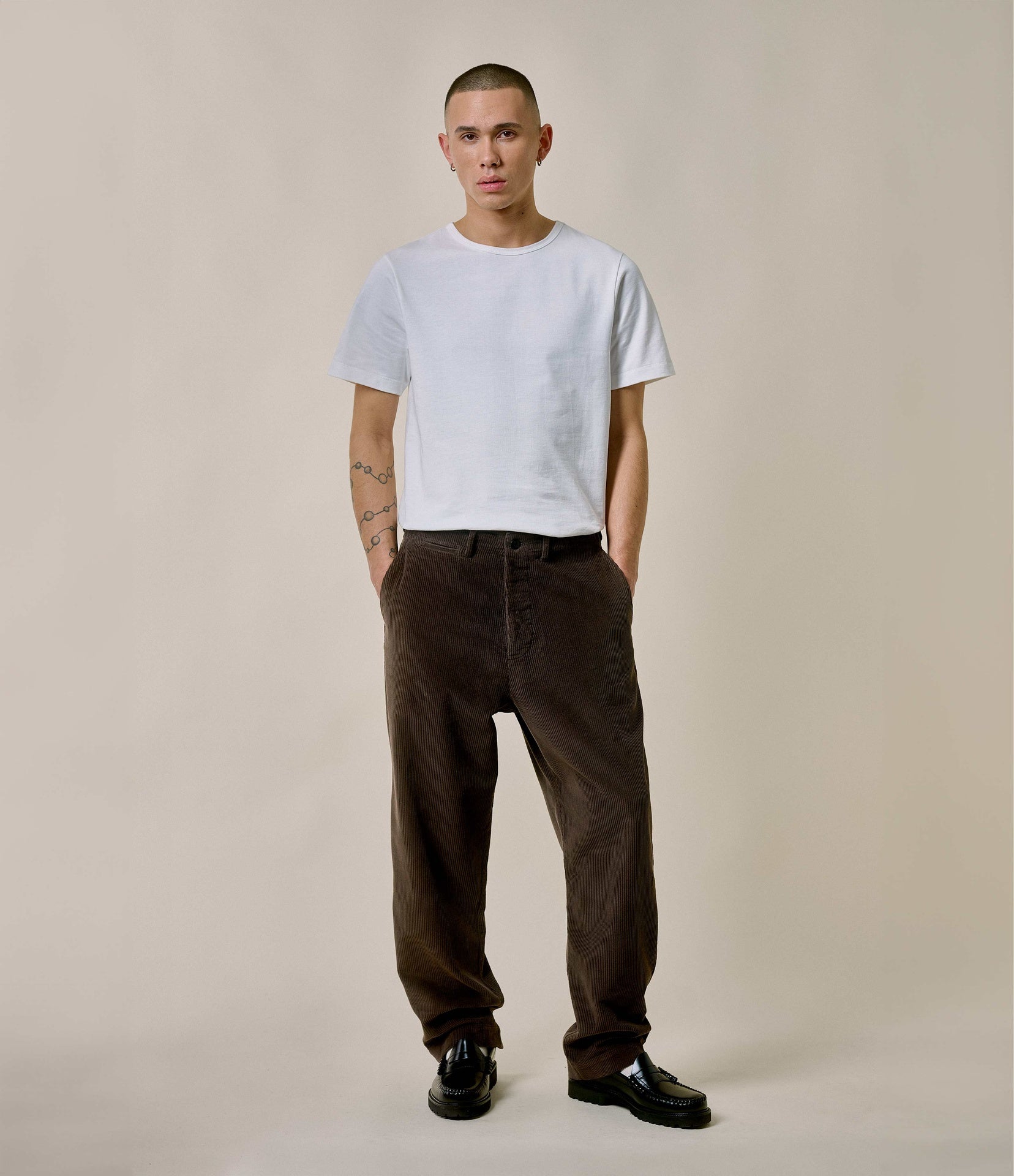 Person wearing a white t-shirt and brown pants against a plain background