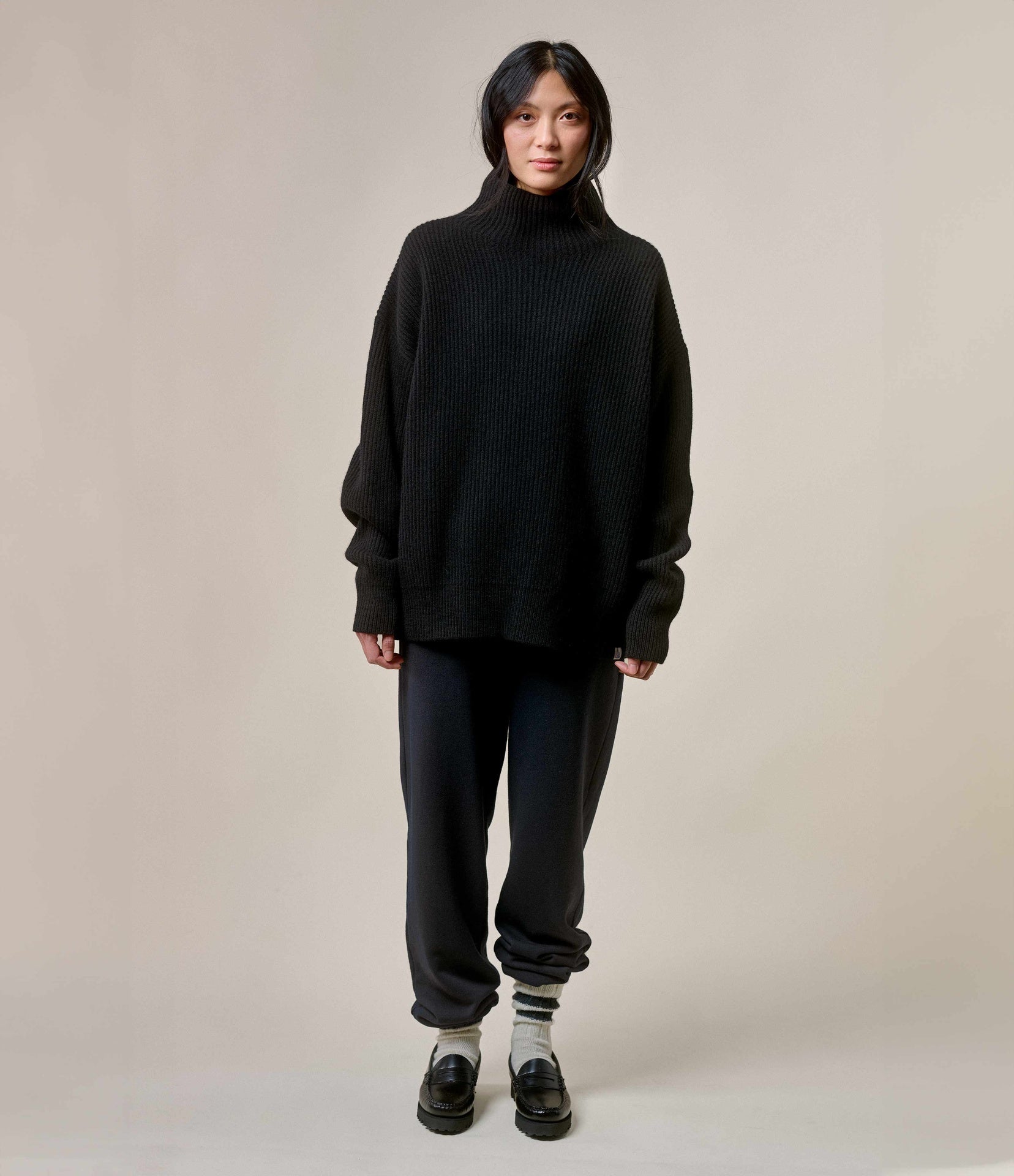 Person wearing a black sweater and pants on a neutral background