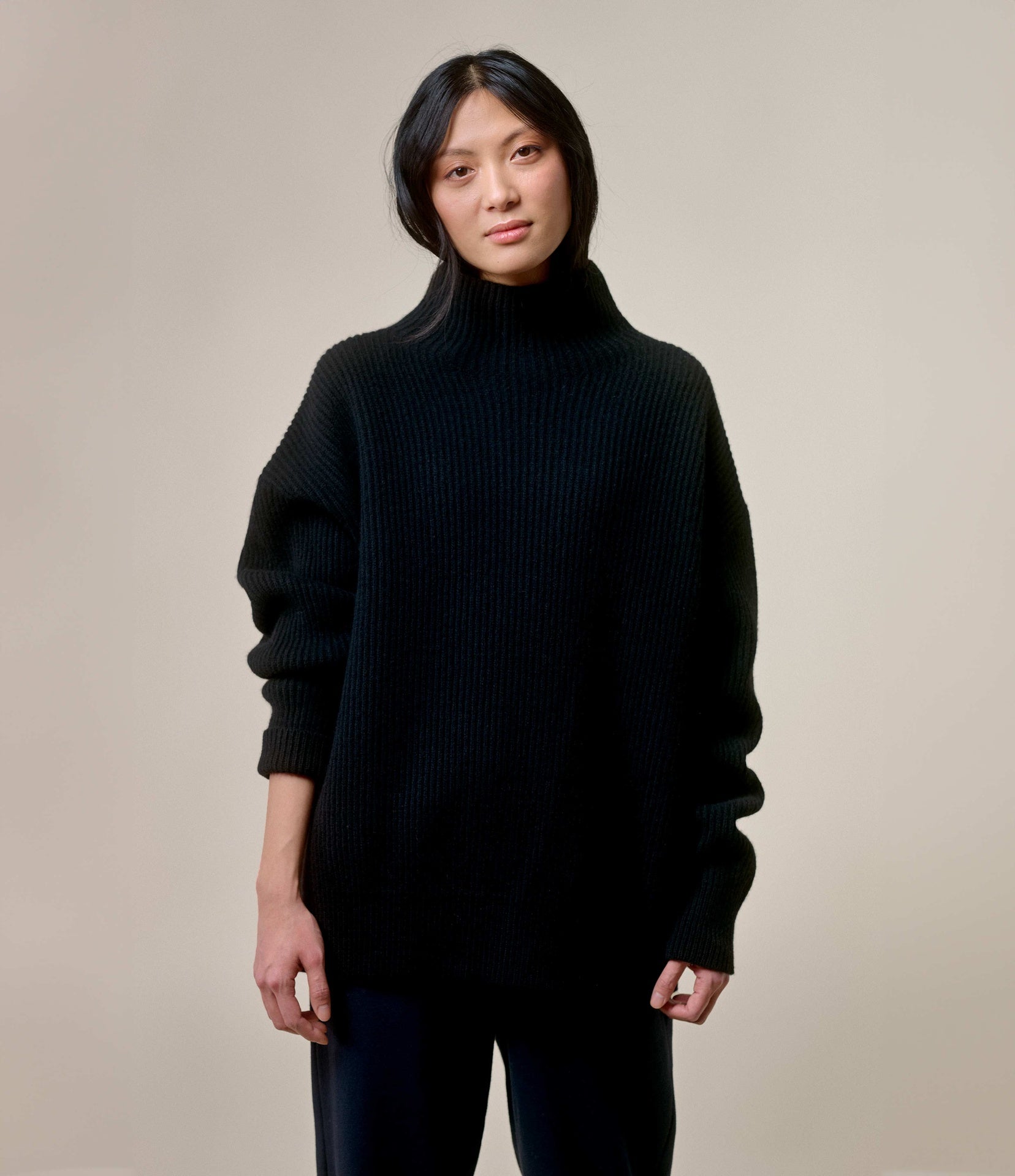 A person wearing a black ribbed merino wool-cashmere mock-neck sweater.