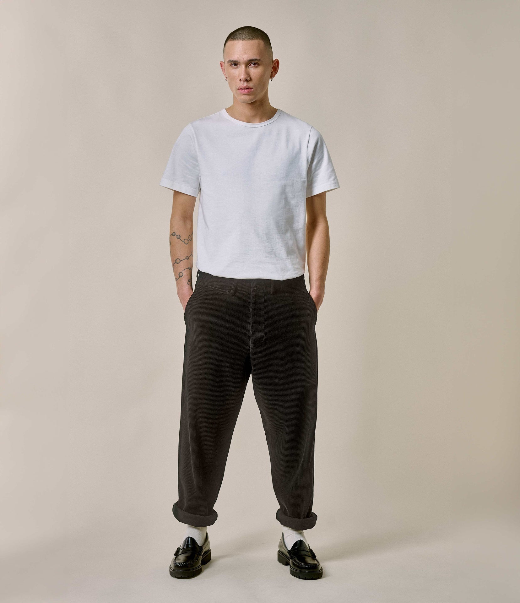 Person wearing a white t-shirt and dark pants against a plain background
