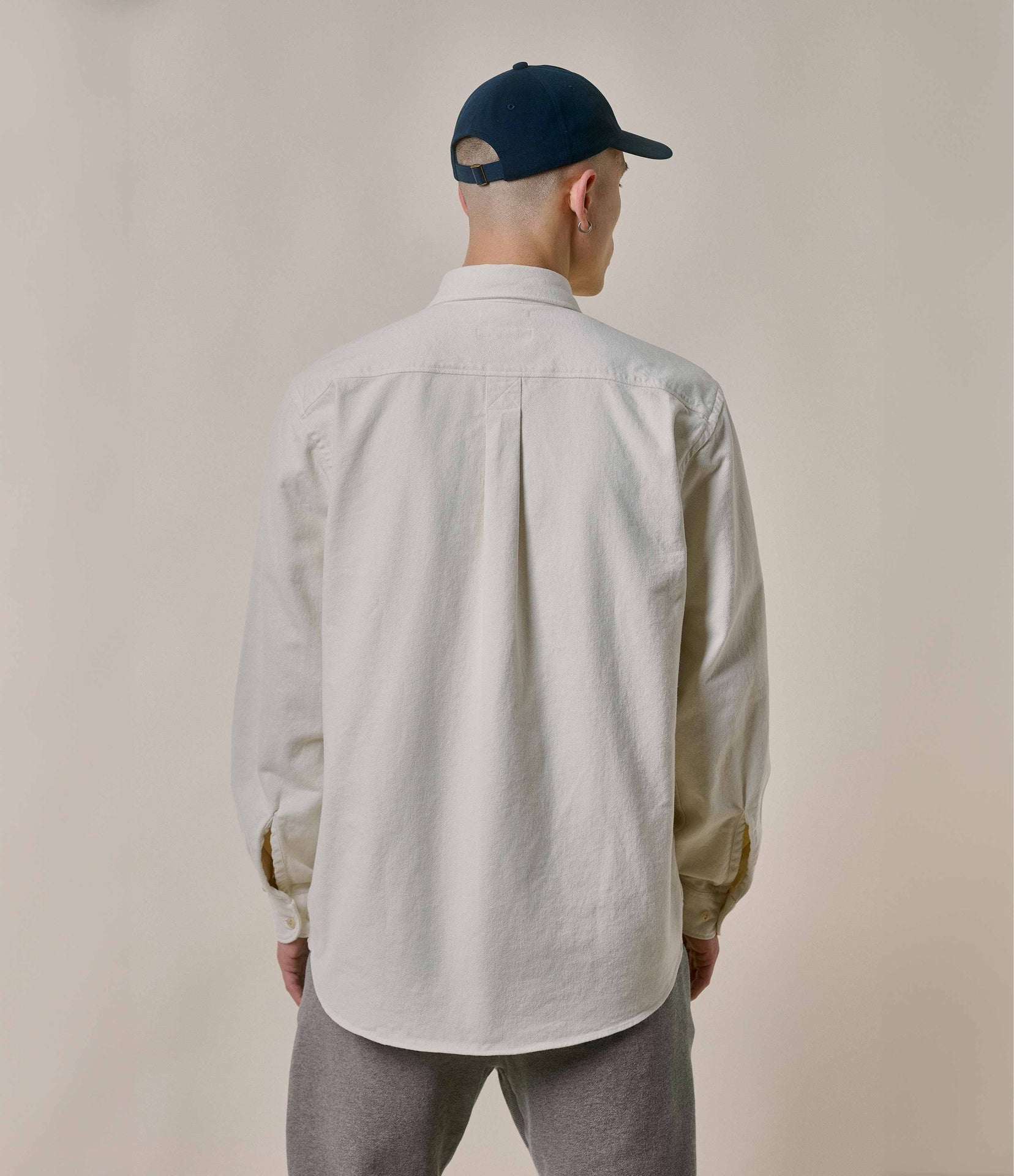 Man weairng beige twill shirt with pleat on the back and a blue cap