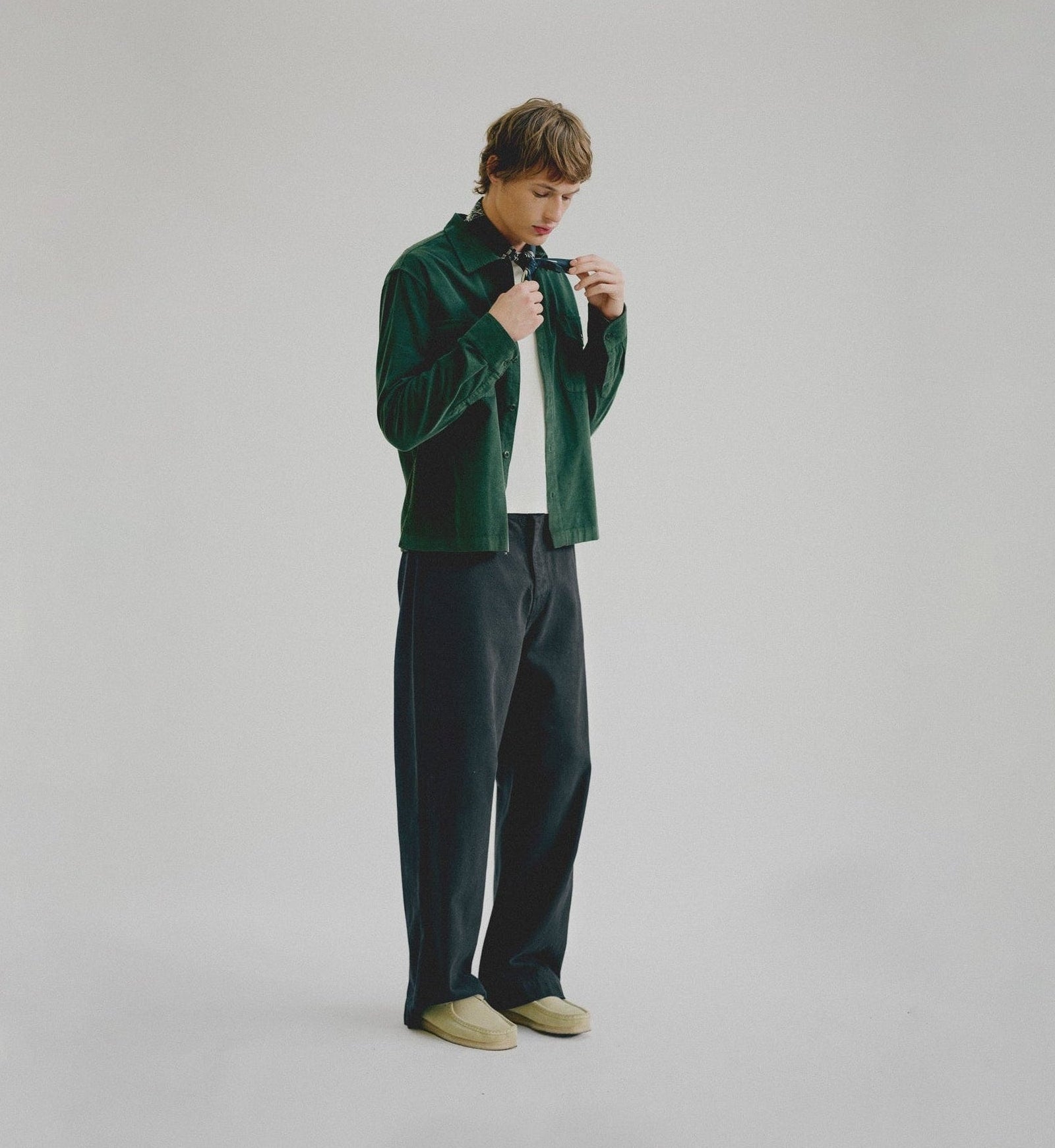Person wearing a green velvet shirt and dark pants on a plain background