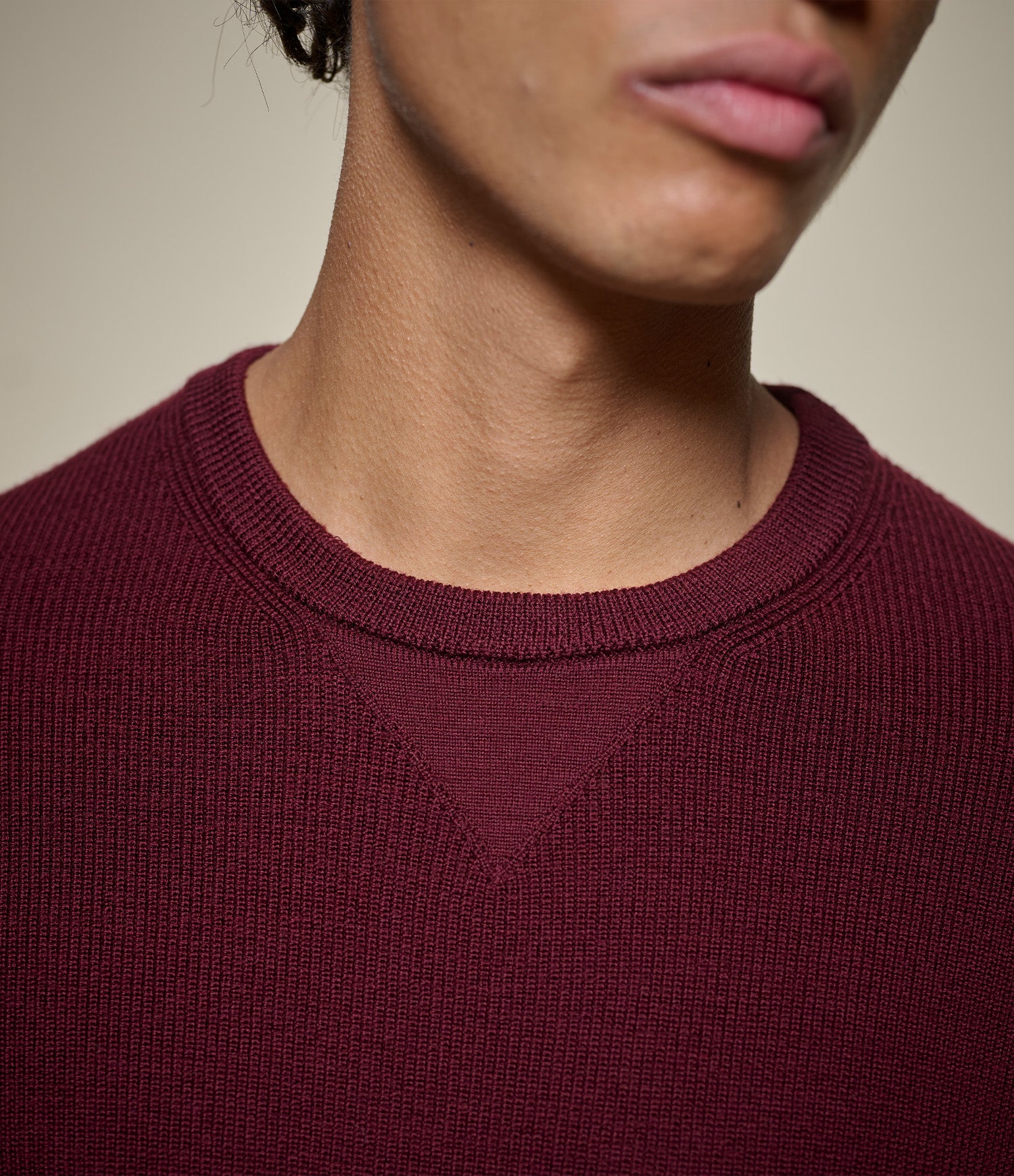 Close-up of a person wearing a maroon sweater with a neutral background