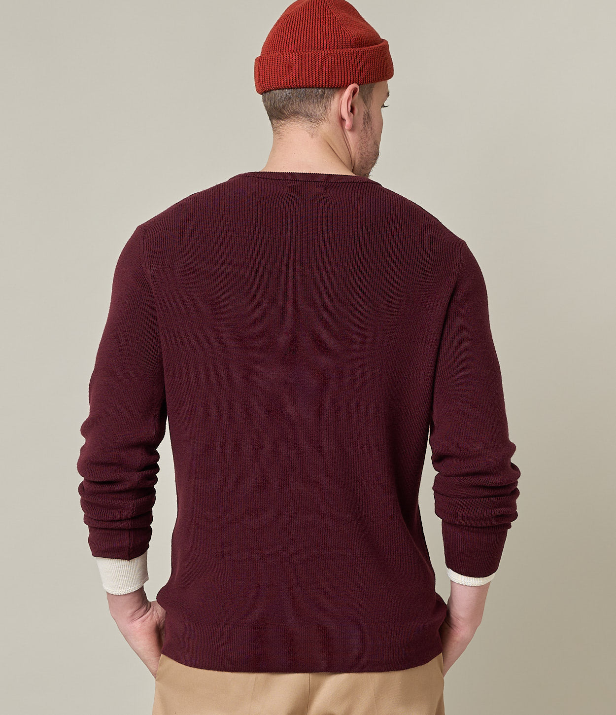 Man wearing a burgundy sweater and red beanie on a beige background