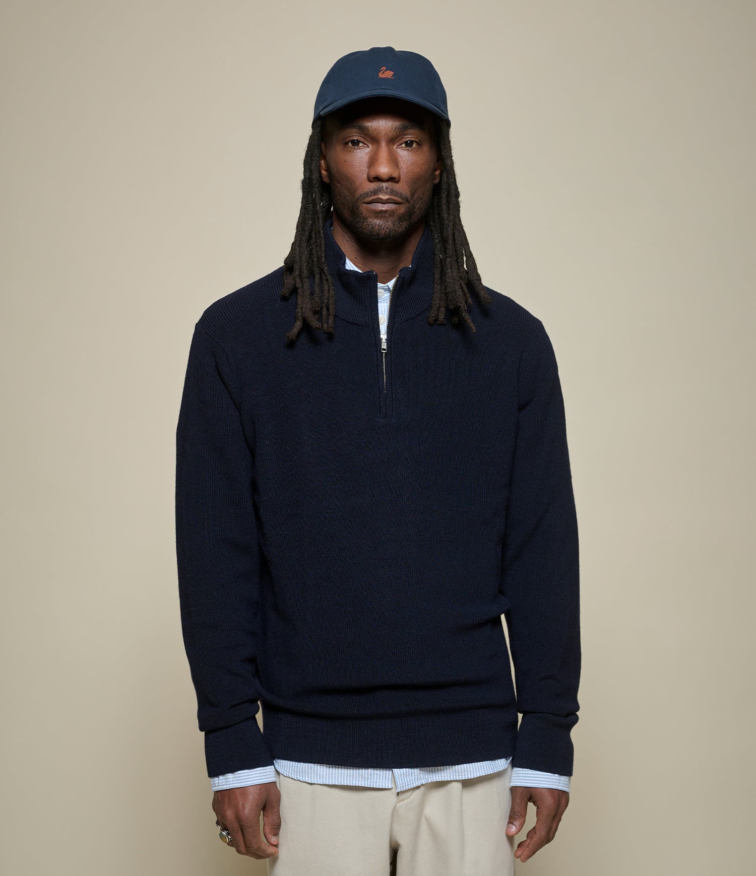 Man wearing a navy blue half-zip sweater and cap against a beige background