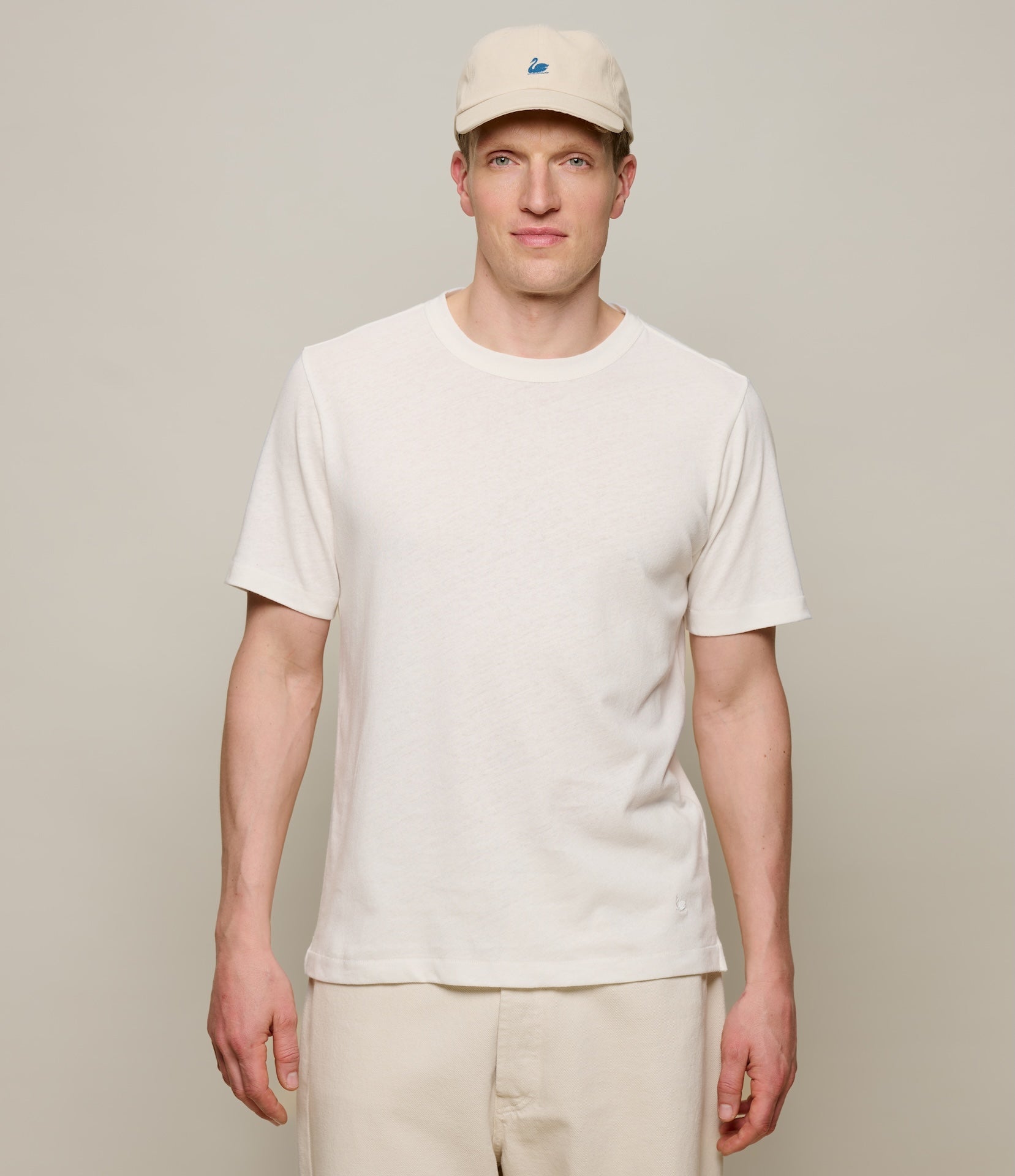 Man wearing a plain white linen t-shirt and beige cap against a neutral background