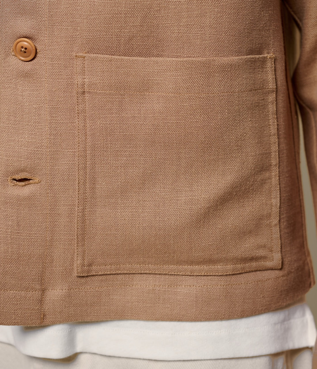 Close-up of a brown linen jacket with a pocket and button detail.