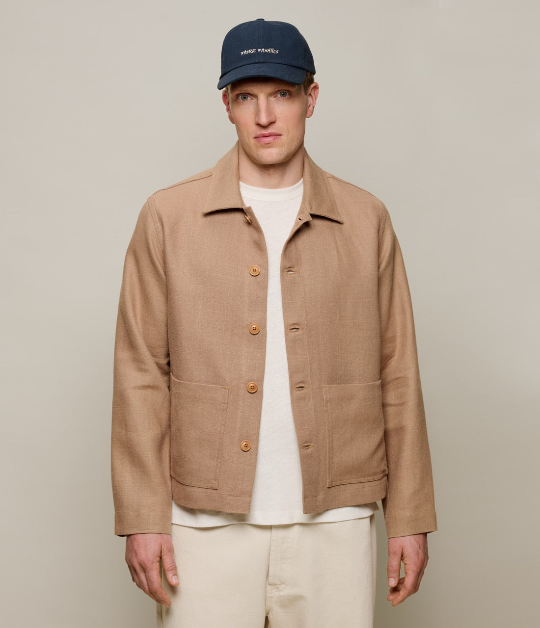 Man wearing a beige linen jacket, white shirt, and navy cap on a plain background