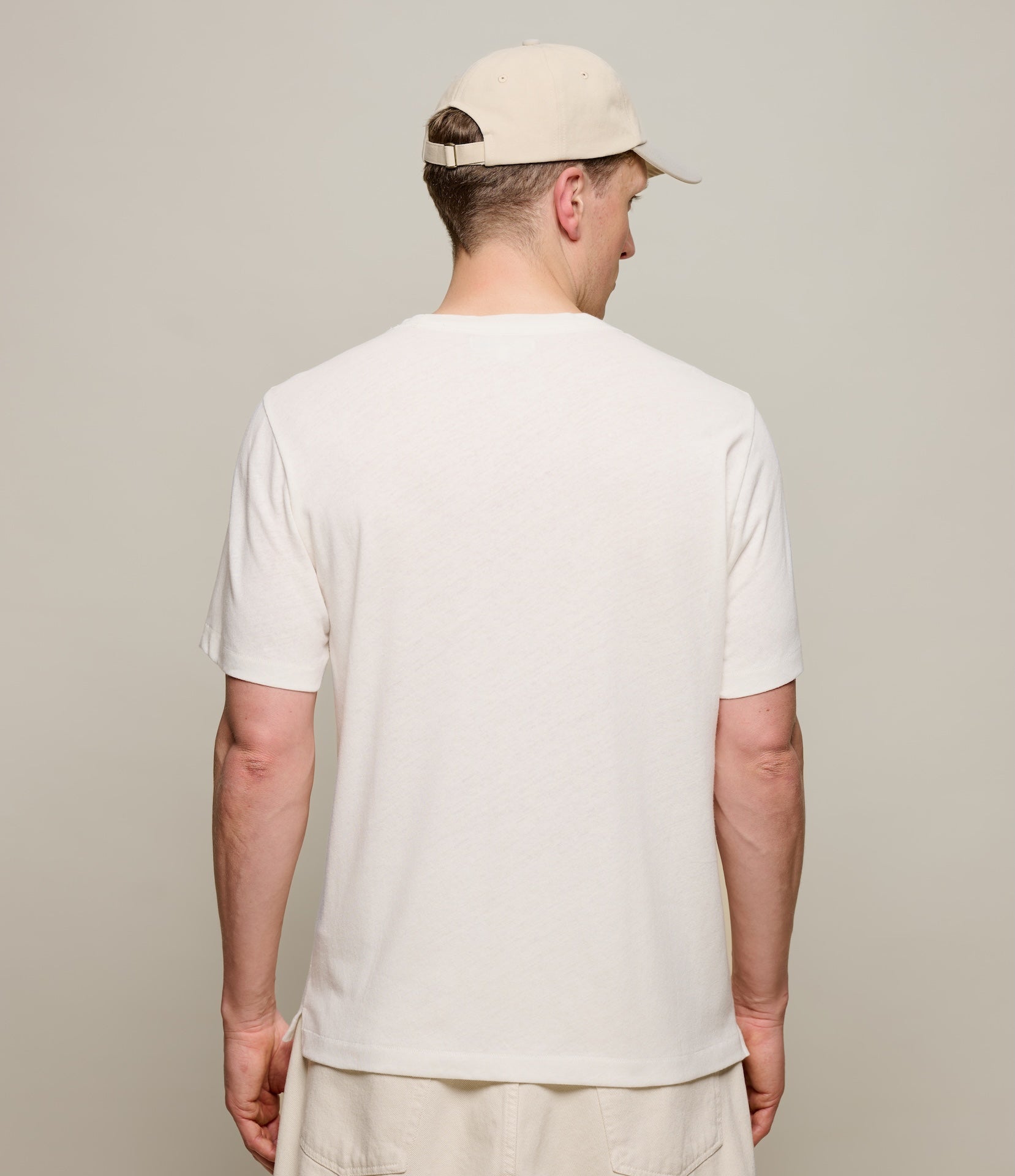 Person wearing a plain white linen t-shirt and beige cap against a neutral background