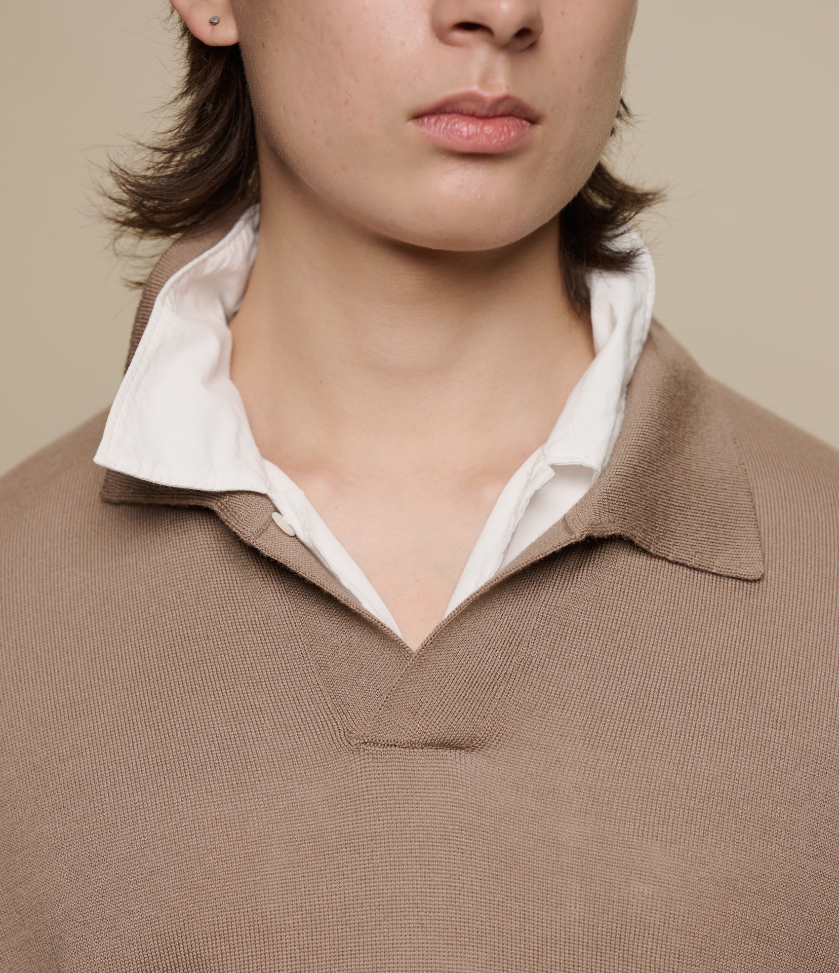 Close-up of a person wearing a brown knitted polo short over a white shirt against a beige background