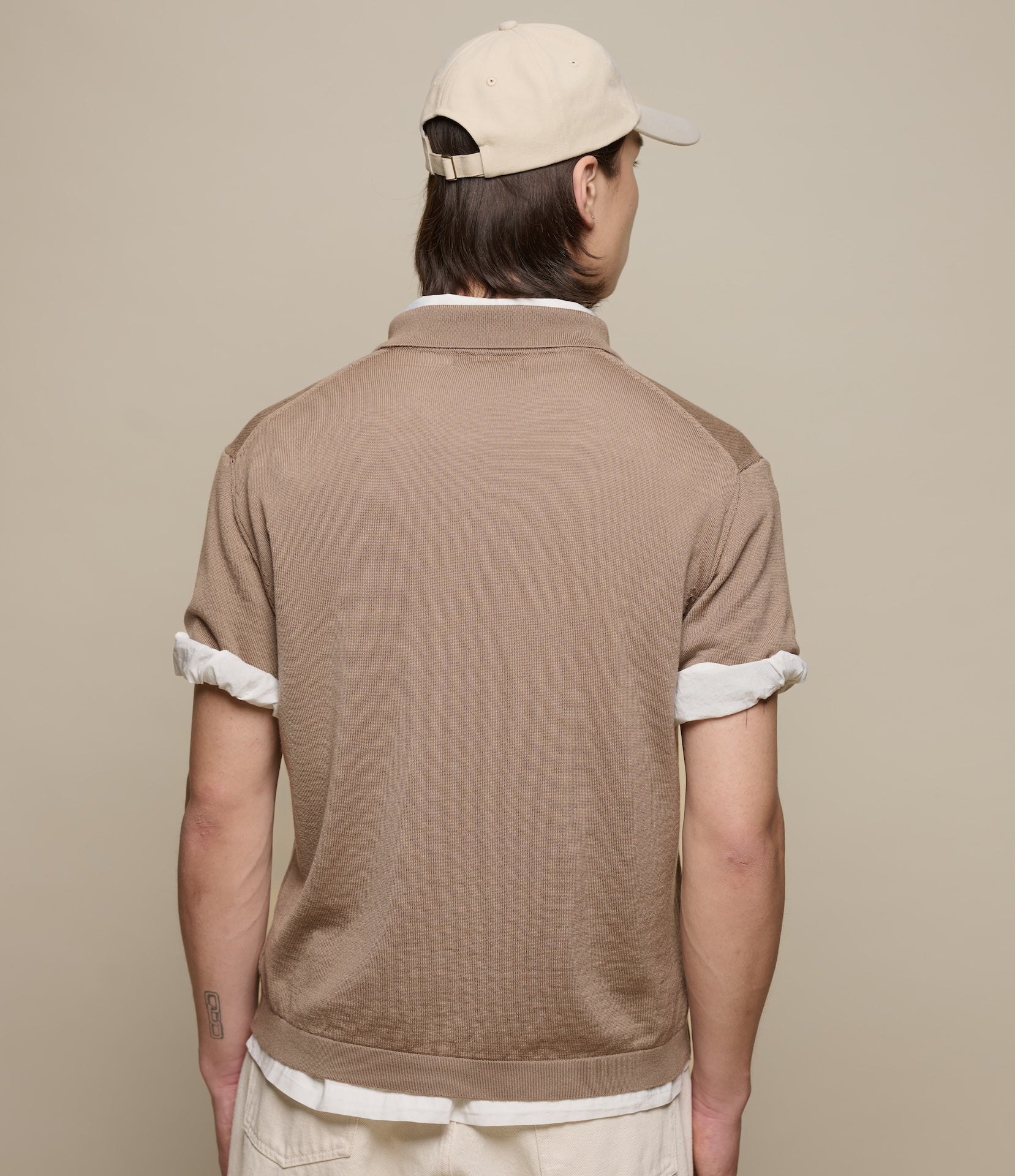 Person wearing a brown knitted polo shirt and beige cap on a beige background