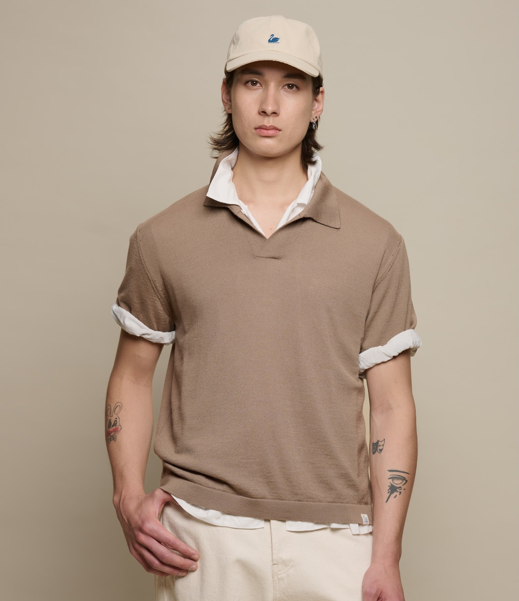 Man wearing a brown knitted merino wool polo shirt and a beige cap against a beige background