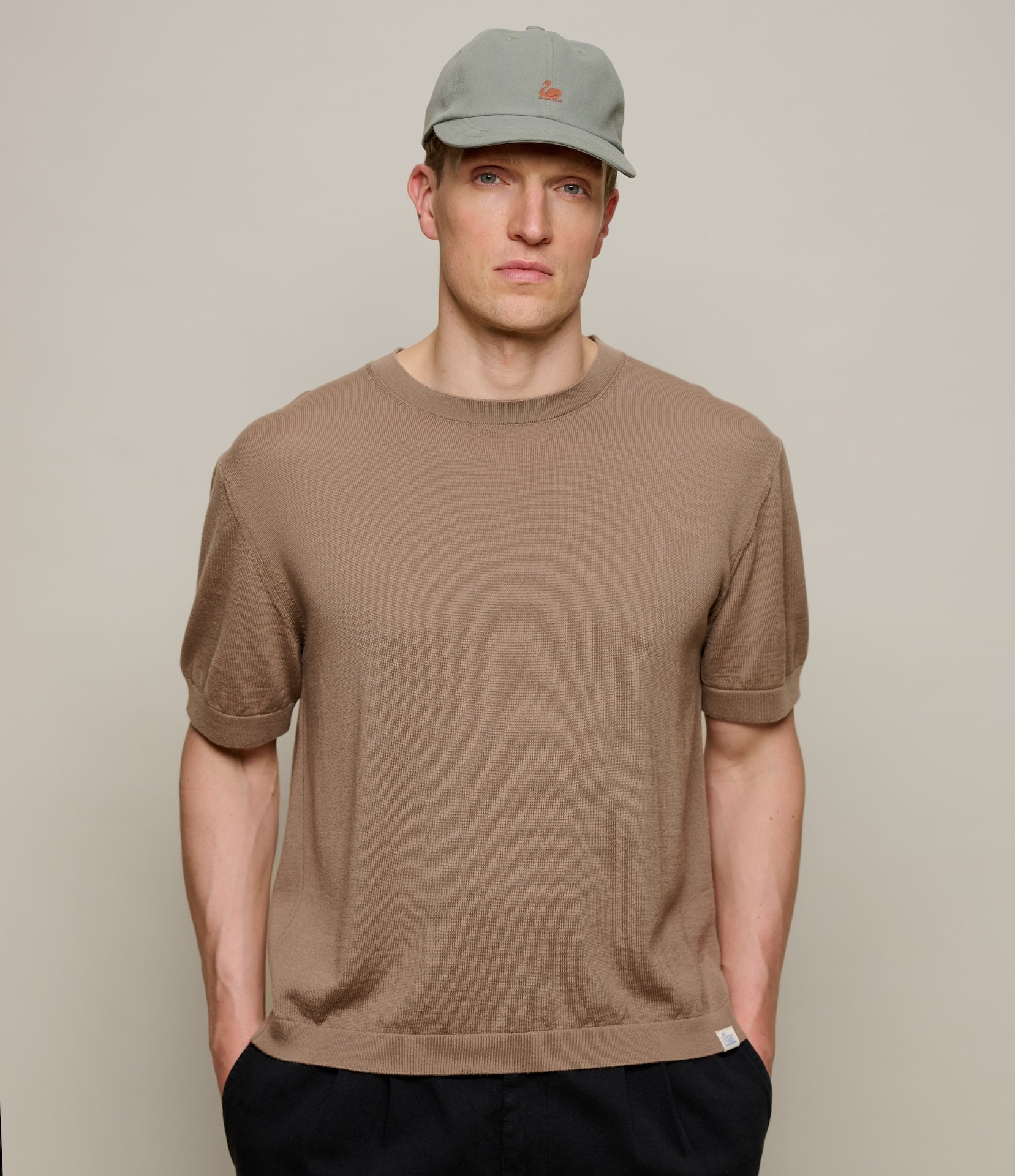 Man wearing a brown knitted merino wool t-shirt and cap against a plain background