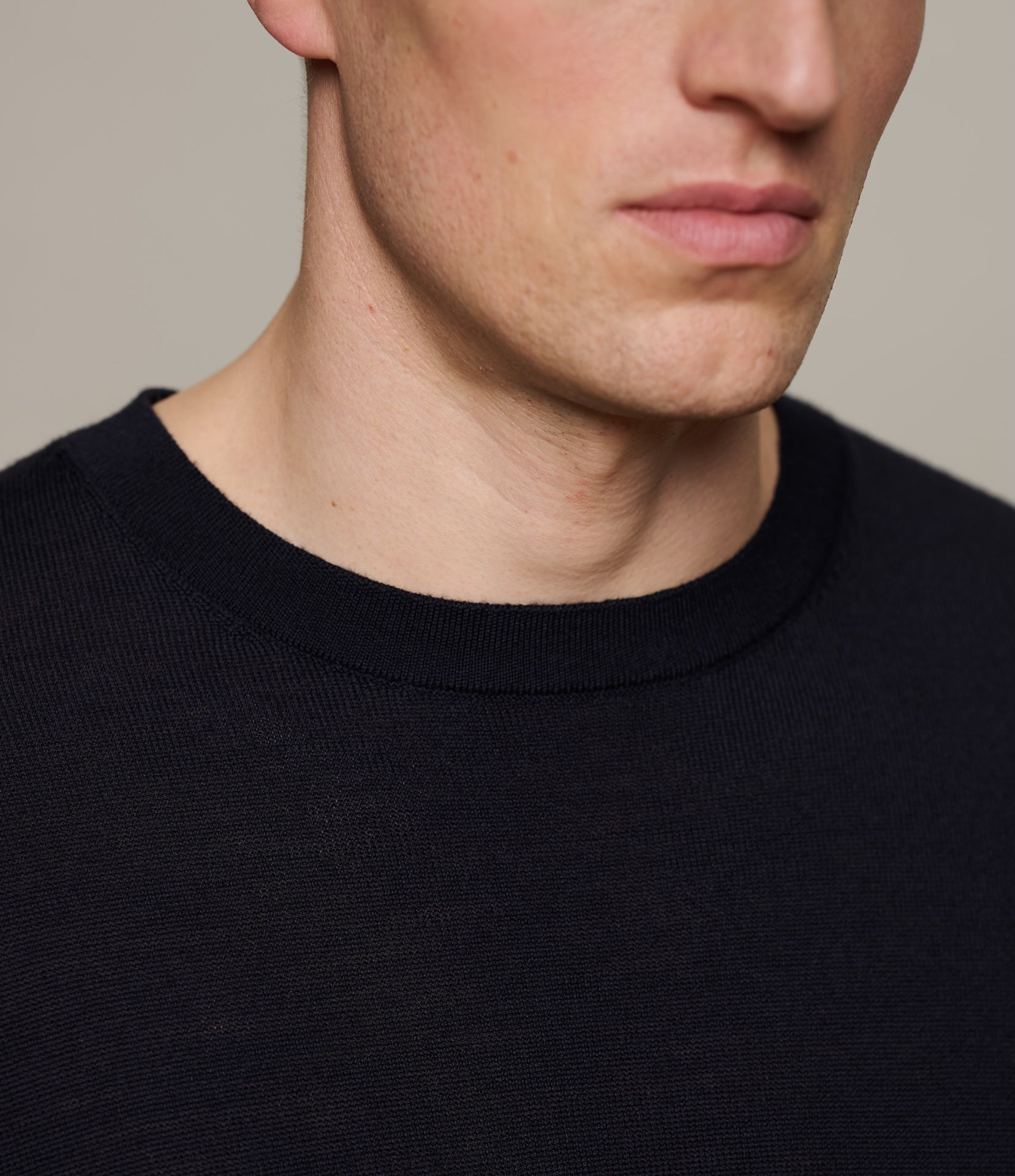 Close-up of a person wearing a dark navy knitted T-shirt against a neutral background