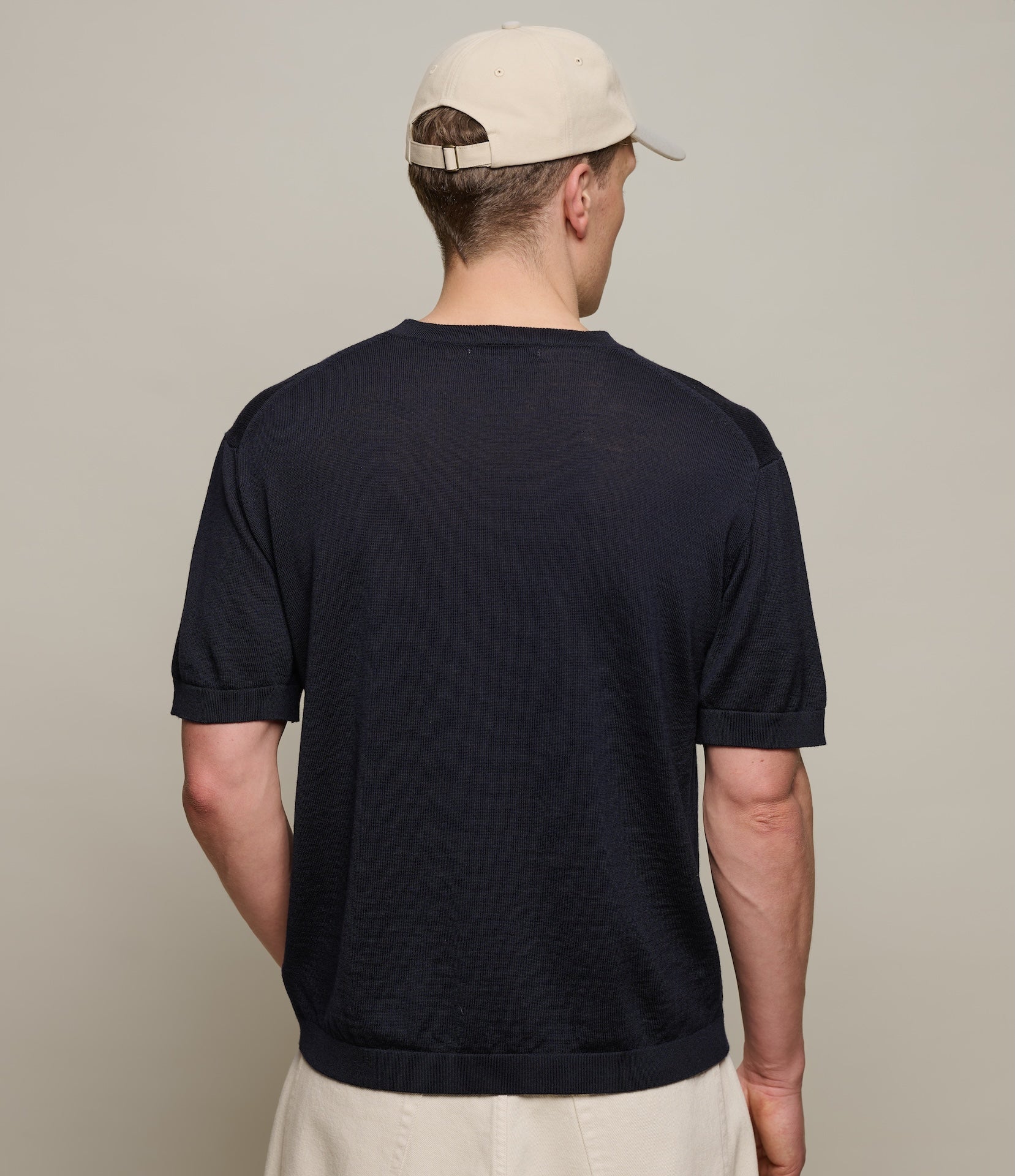 Man wearing a dark navy t-shirt and beige cap from behind on a plain background