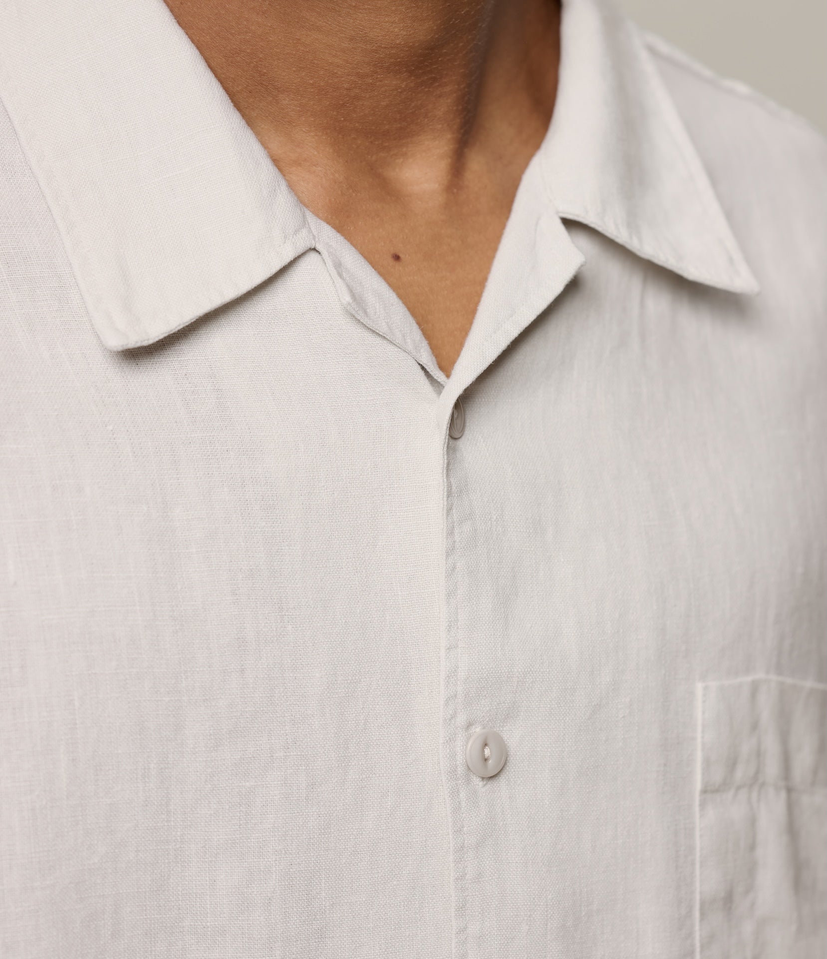 Close-up of a light-colored shirt with an open bowling shirt collar and button detail.