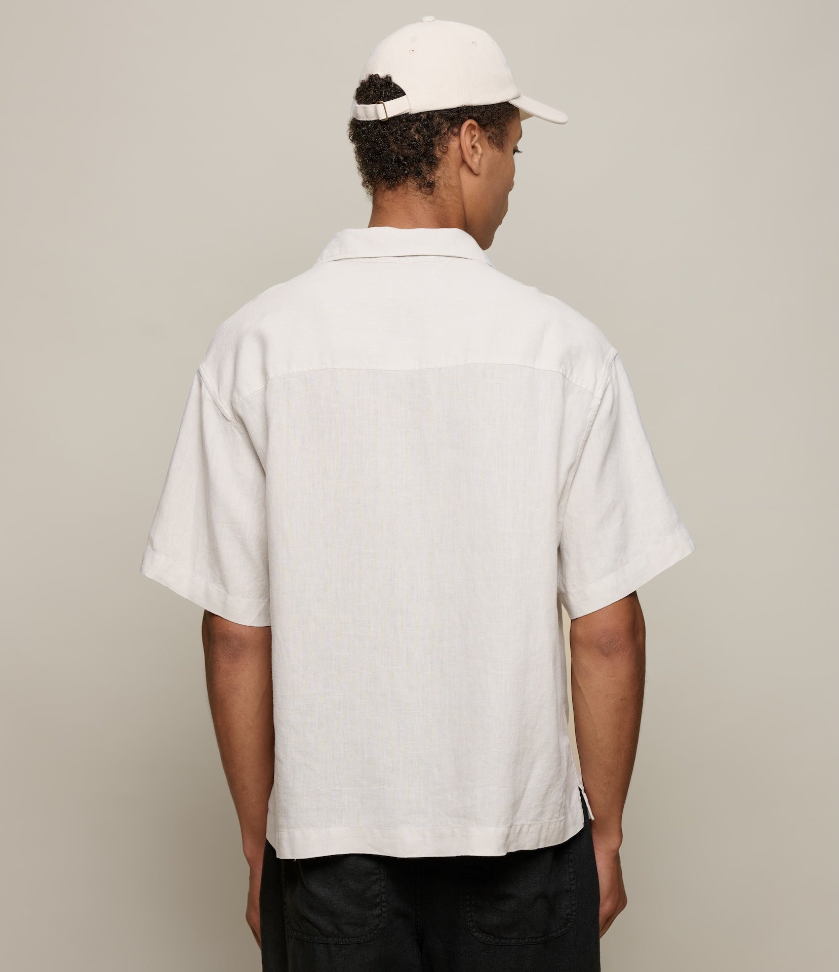 Person wearing a beige linen shirt and cap from behind on a plain background