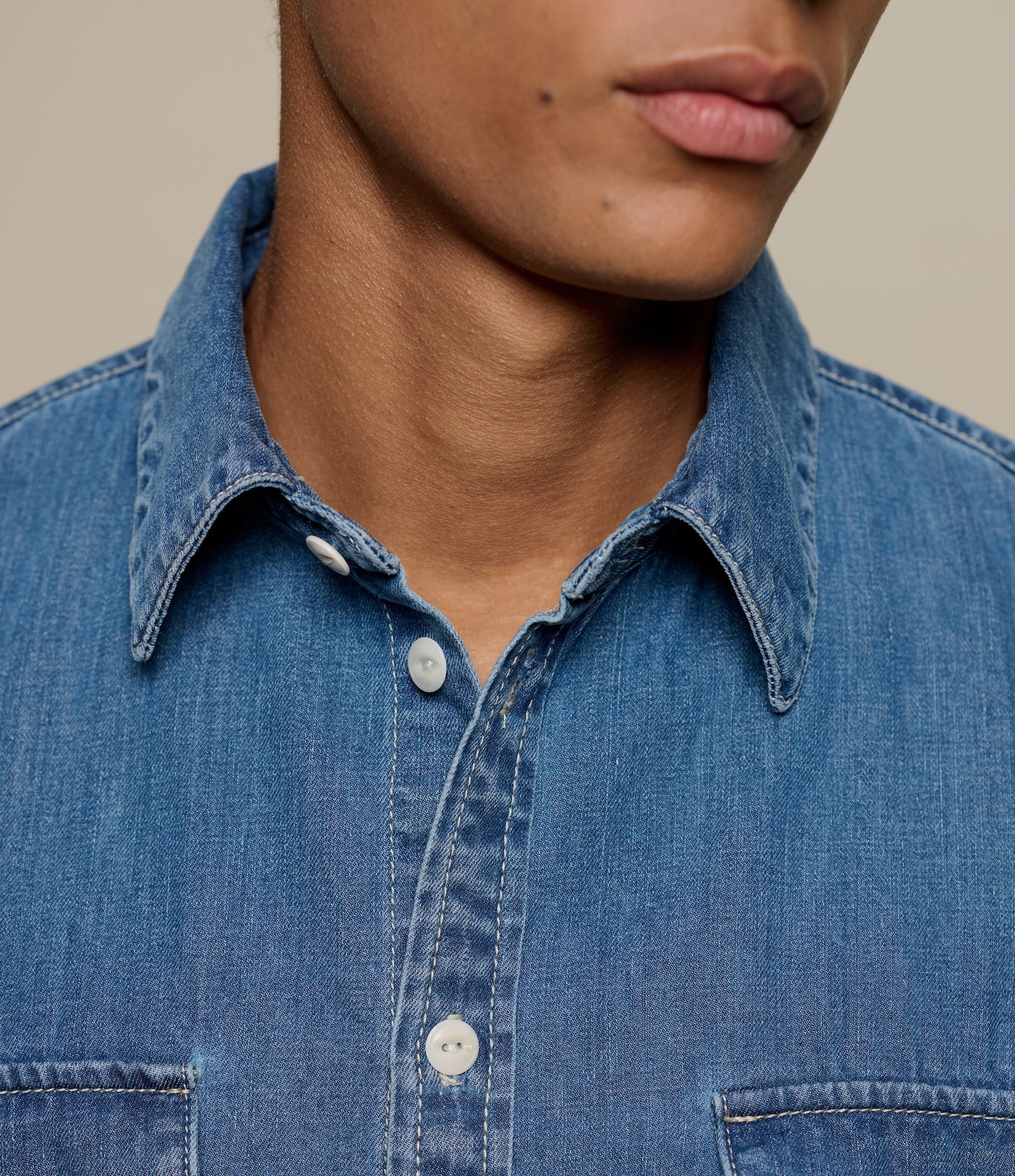 Close-up of a person wearing a blue denim shirt against a neutral background