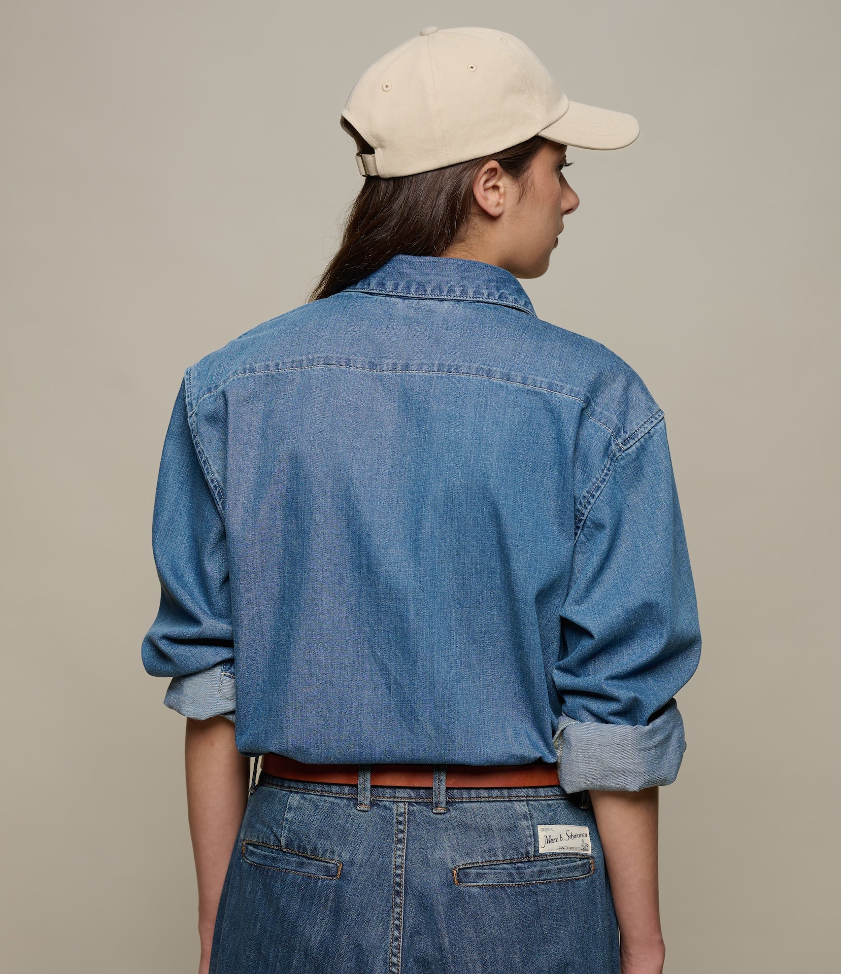 Person wearing a blue denim shirt and beige cap on a plain background