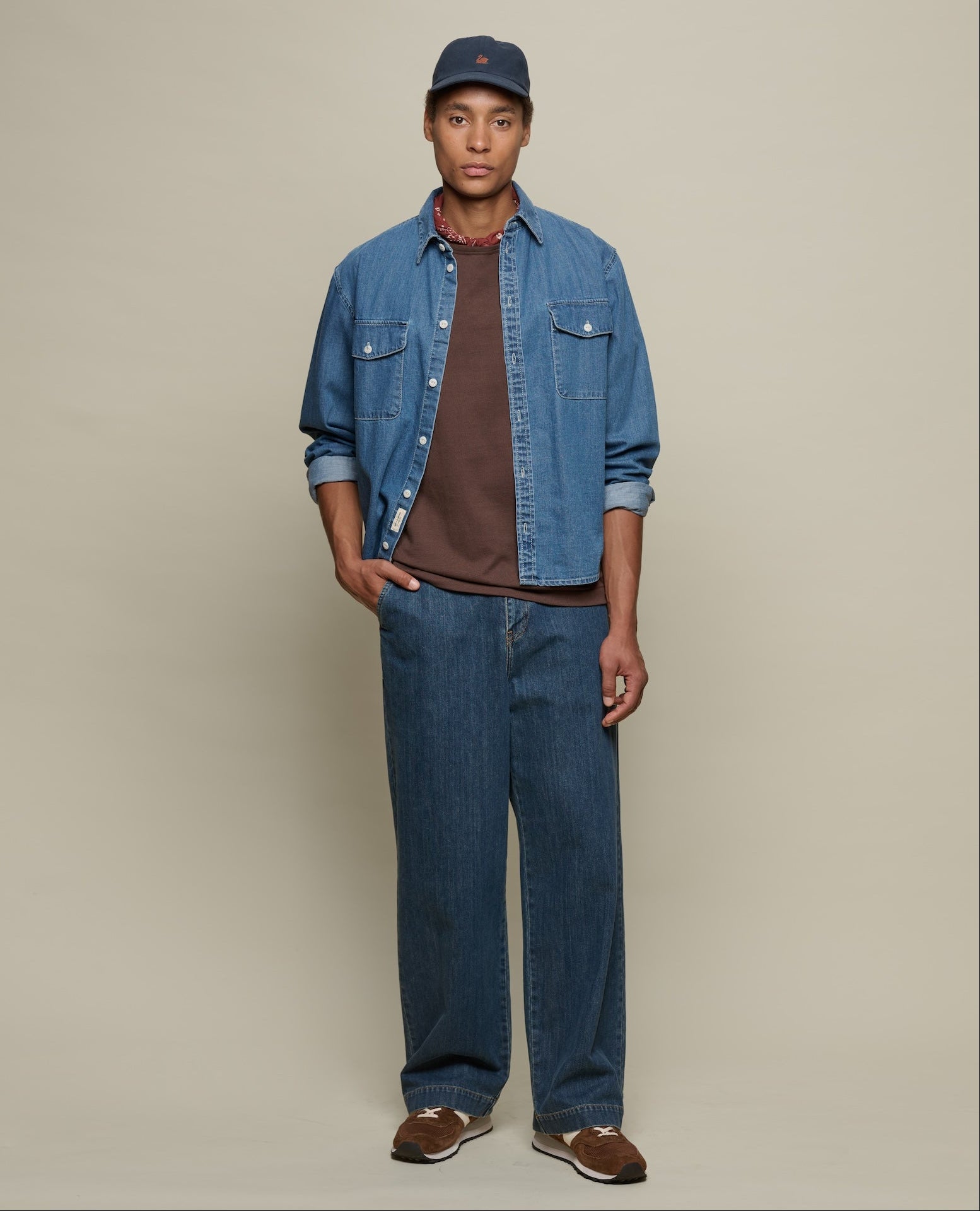Man wearing a denim jacket, cap, and jeans on a plain background