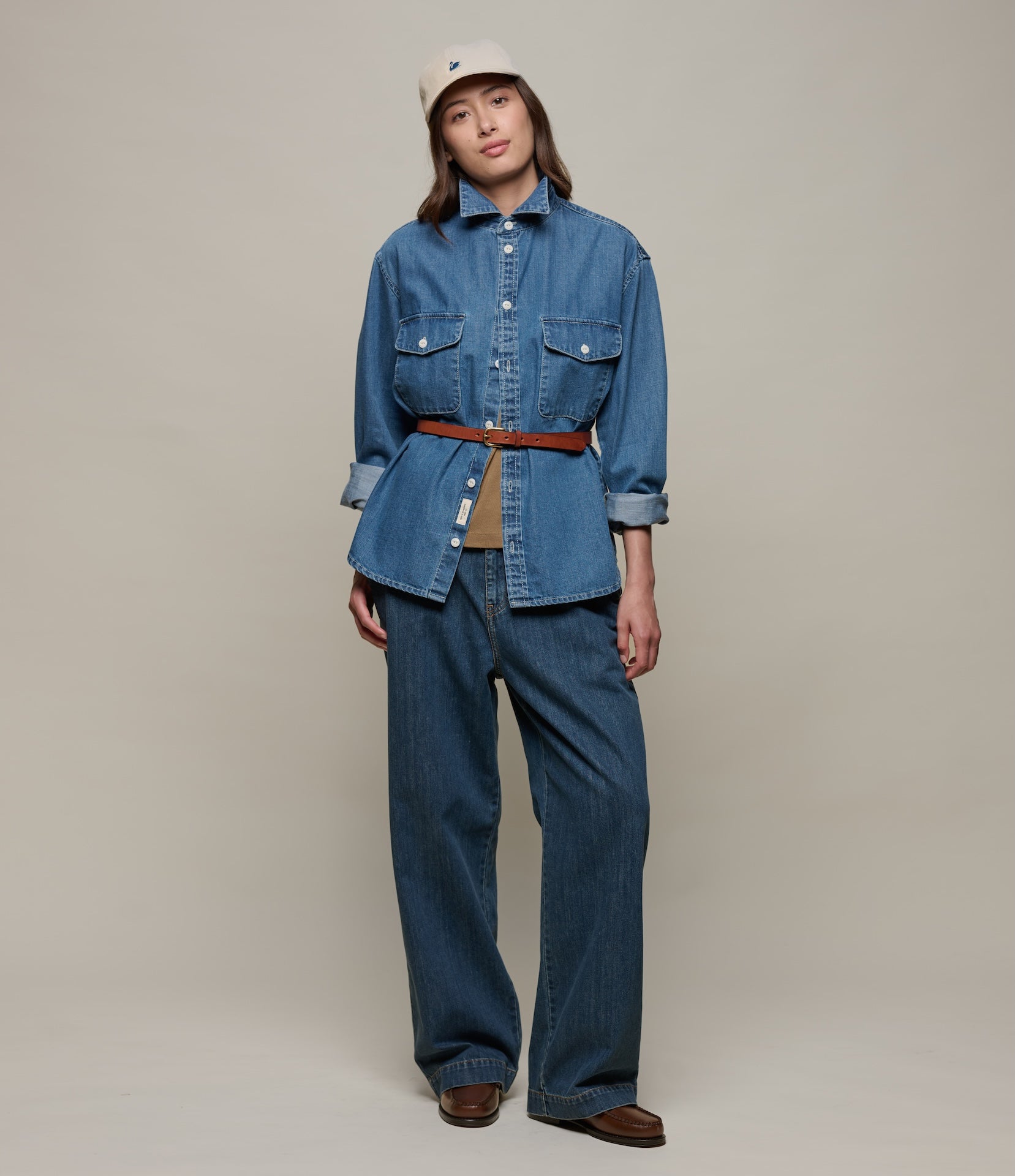 Person wearing a blue denim outfit with a beige cap on a plain background