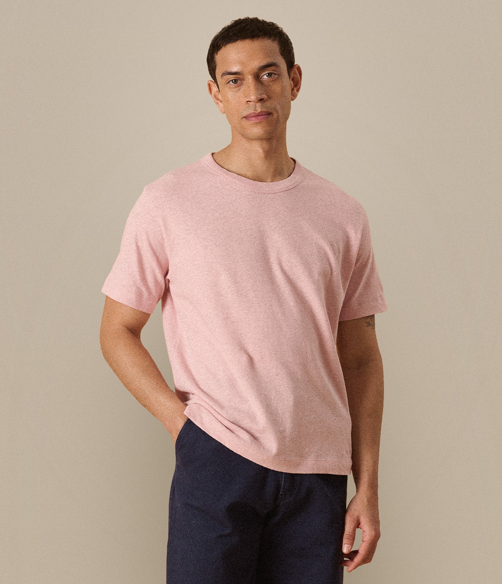 Man wearing a pink lijnen/cotton t-shirt and dark pants against a beige background