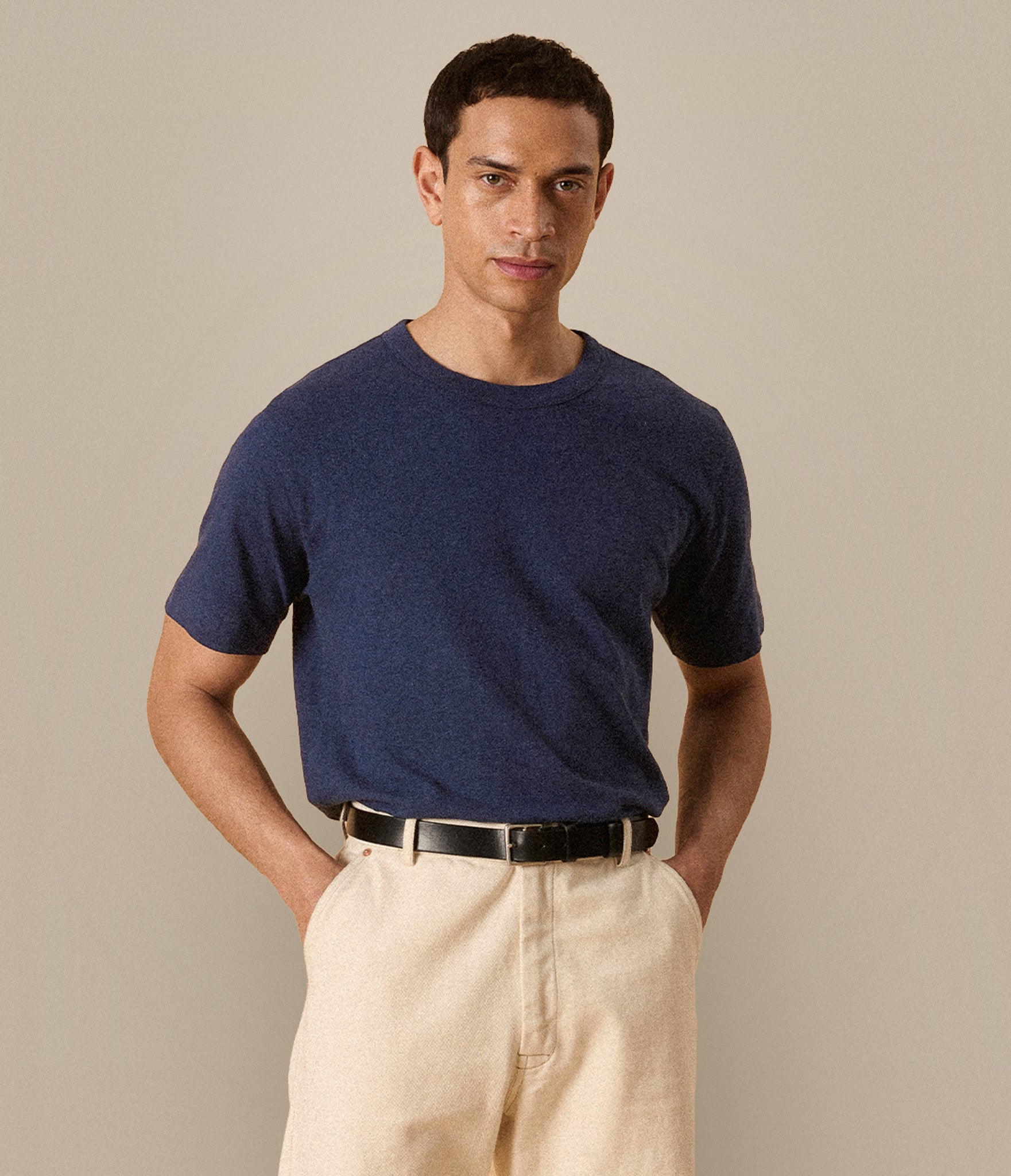 Man wearing a navy blue linen/cotton t-shirt and beige pants against a plain background