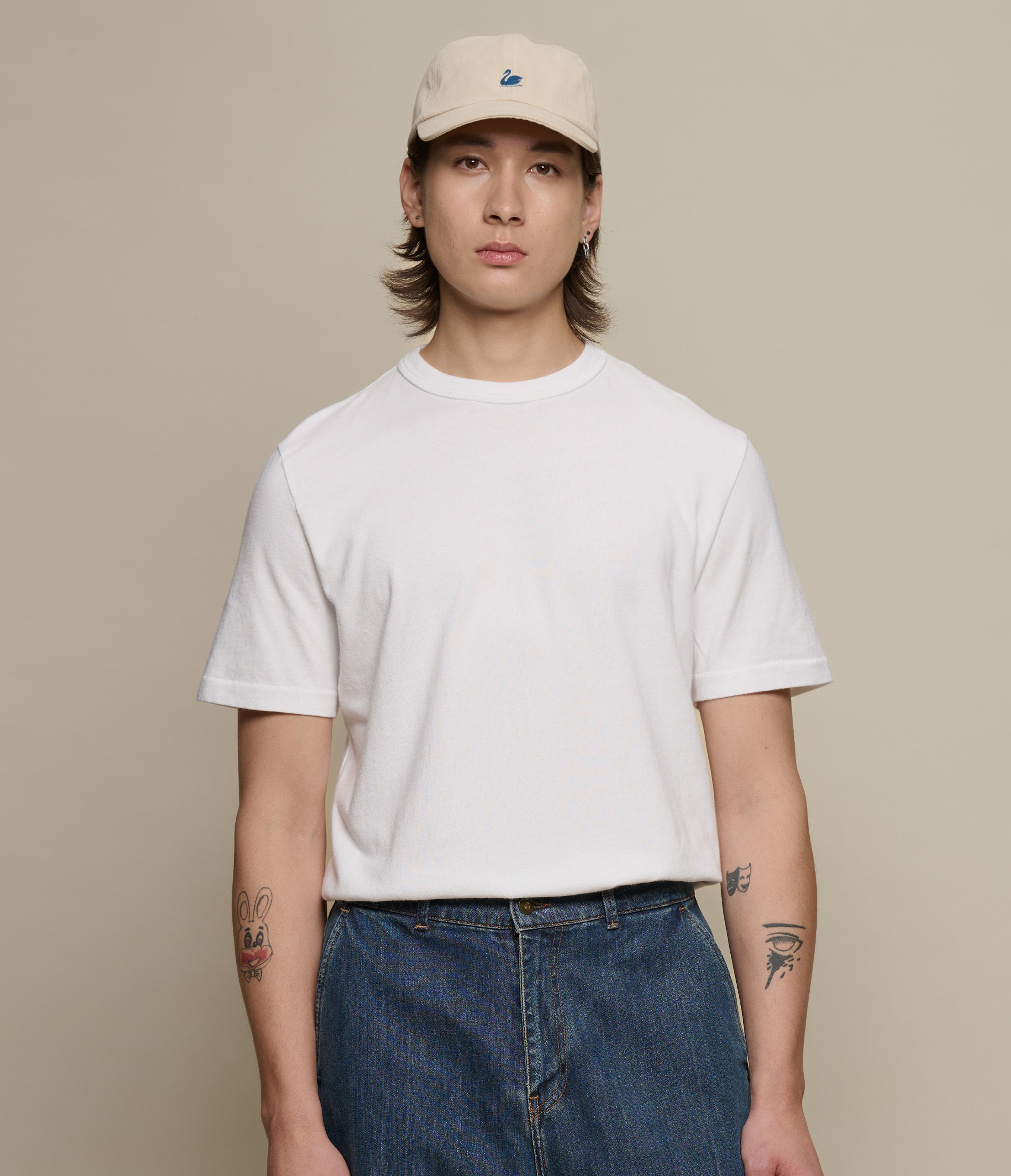 Person wearing a white authentic jersey t-shirt and beige cap on a beige background